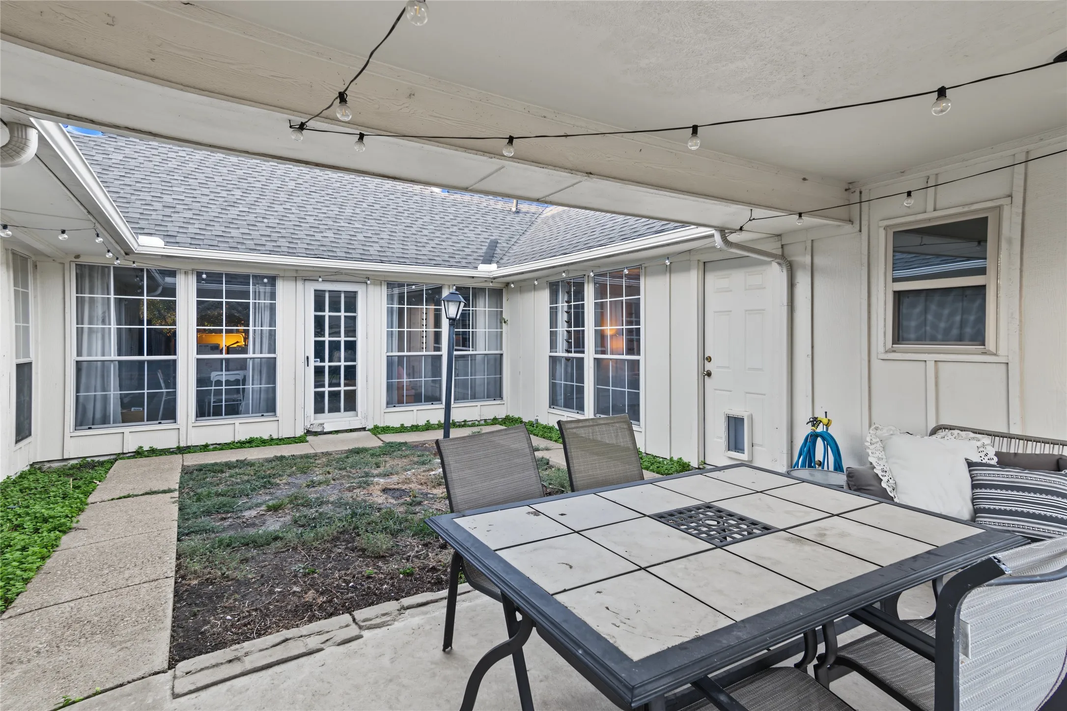 Covered patio with string lighting, direct access to the interior, and a paved walkway