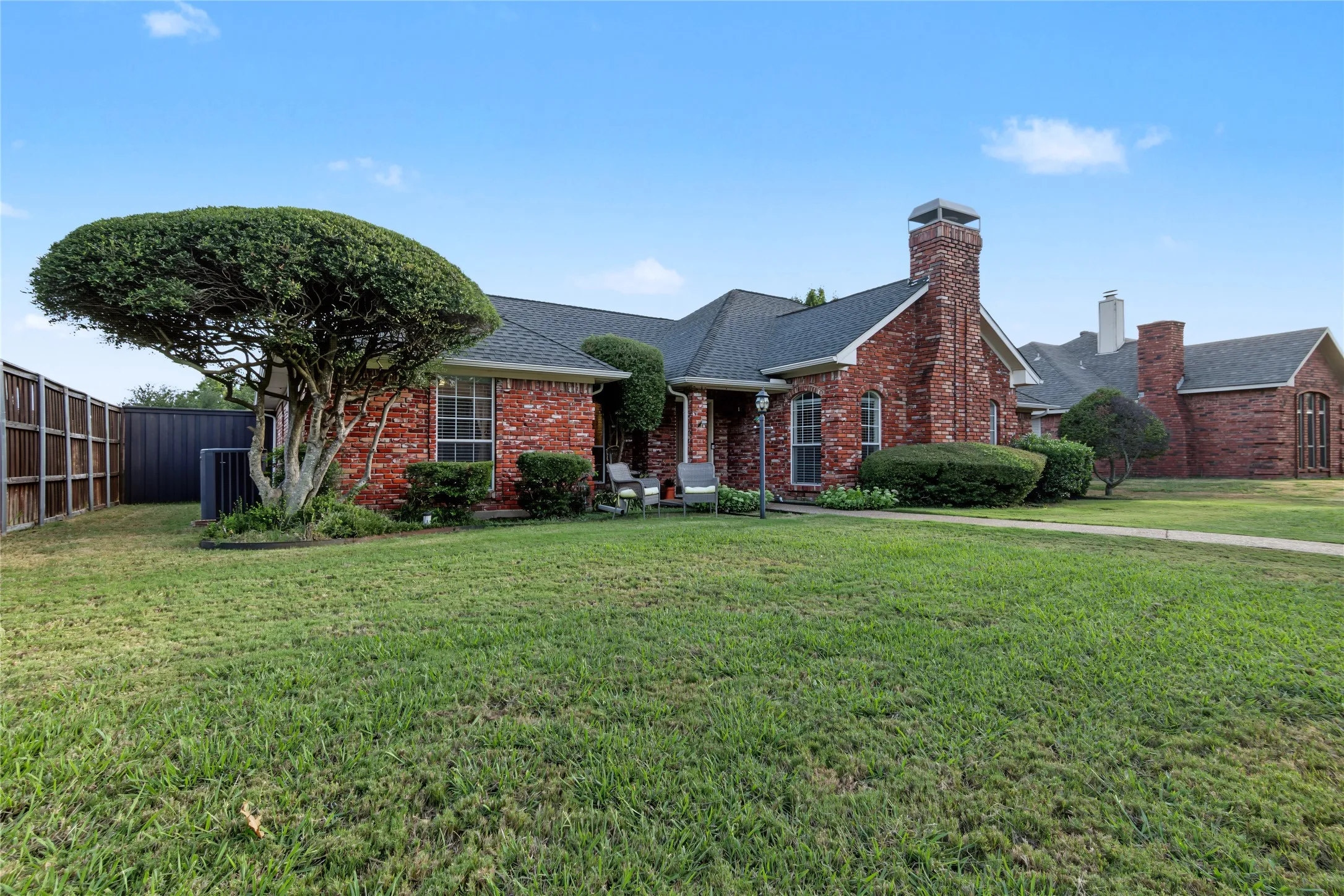 Red brick exterior with multiple chimneys, mature landscaping, fenced side yard, and a paved walkway