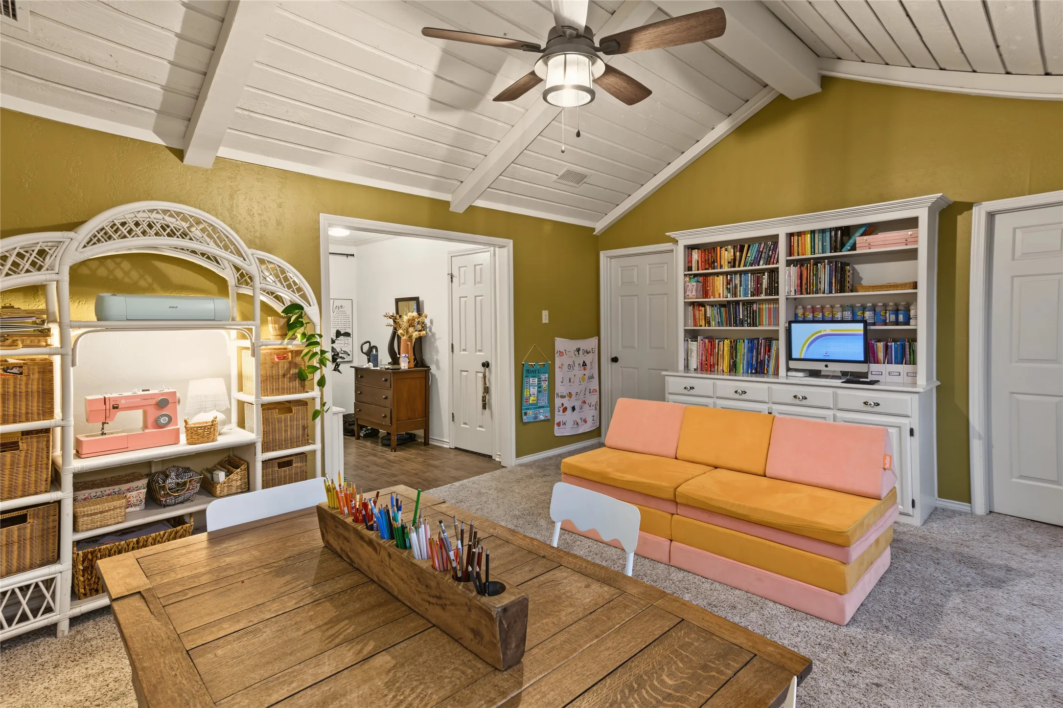 Vaulted ceiling with exposed beams, central ceiling fan, built-in shelving unit, and multiple doors