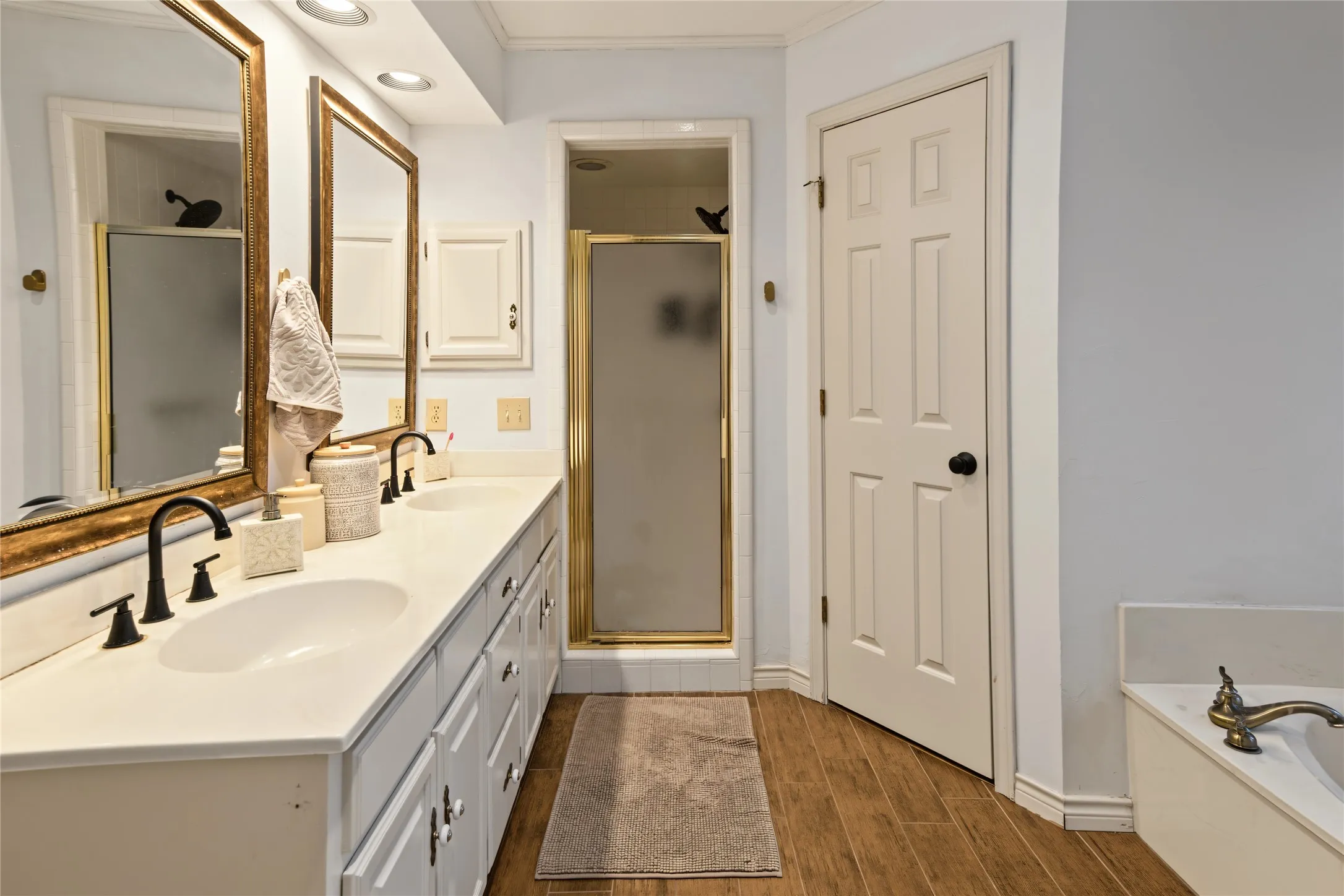 Dual vanity with undermount sinks, wood-finish flooring, shower enclosure with frosted glass, and a built-in soaking tub
