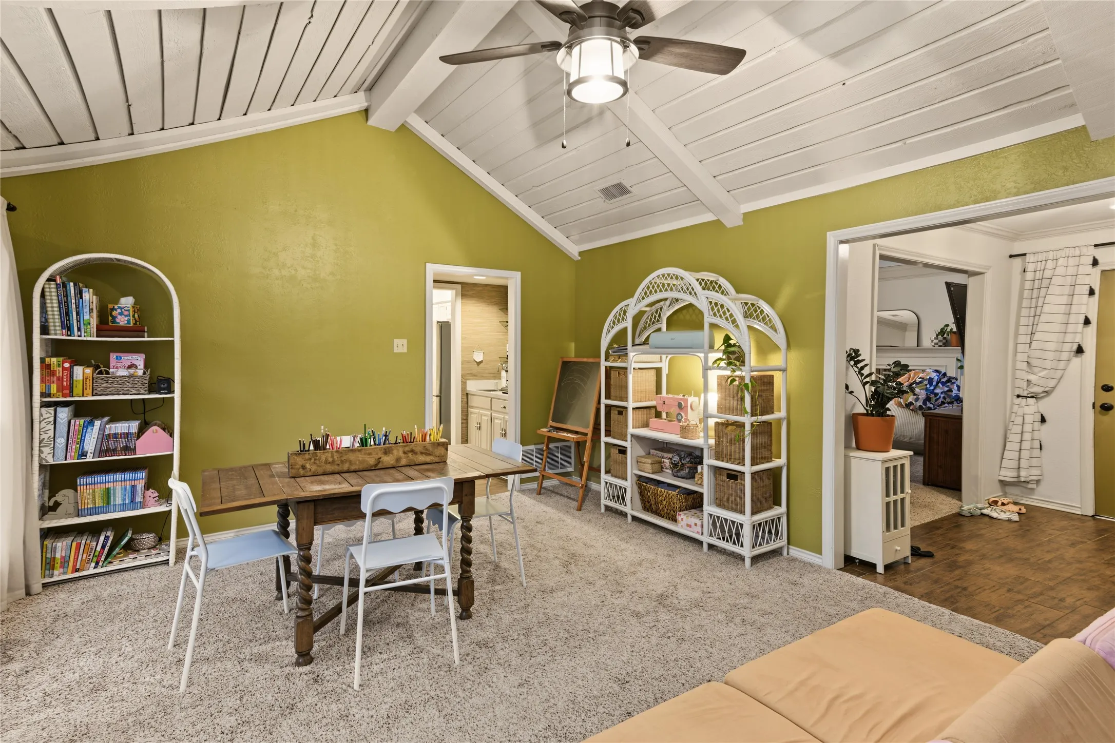 Vaulted ceiling with exposed beams, ceiling fan light fixture, carpeted flooring, and a doorway leading to an additional space