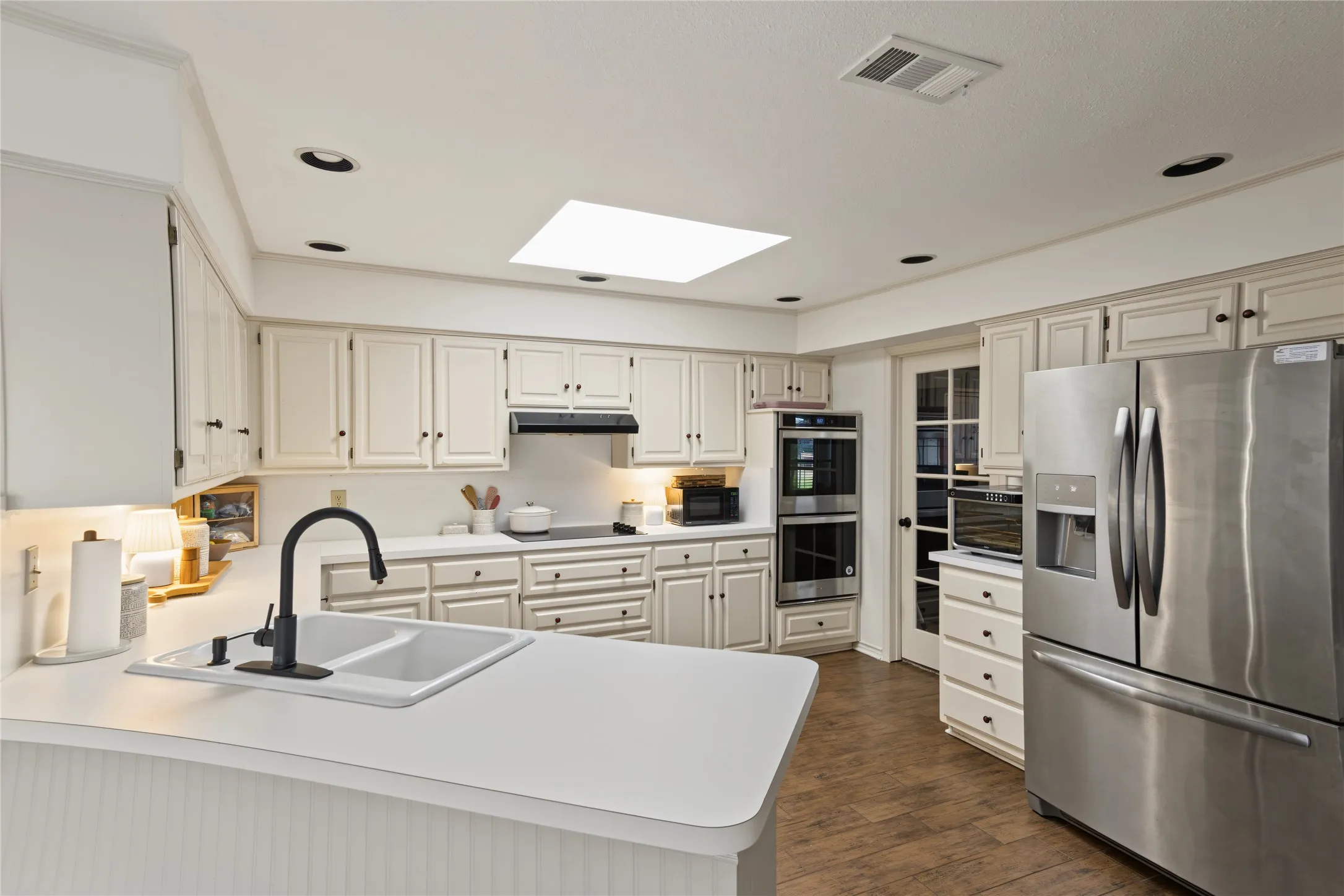 Kitchen with white cabinetry, stainless steel appliances, a double wall oven, and wood-finish flooring