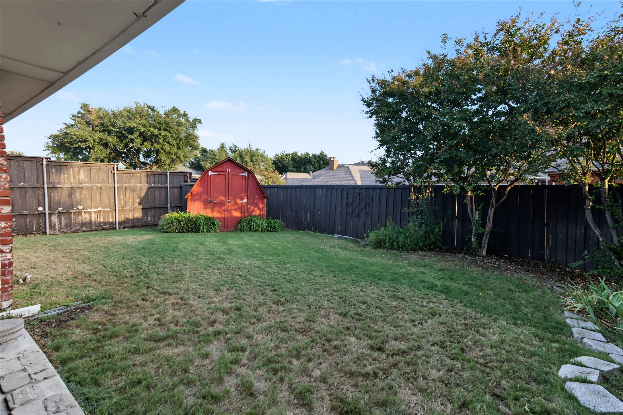 Expansive backyard featuring a manicured lawn, established trees, a red storage shed, and a stone walkway