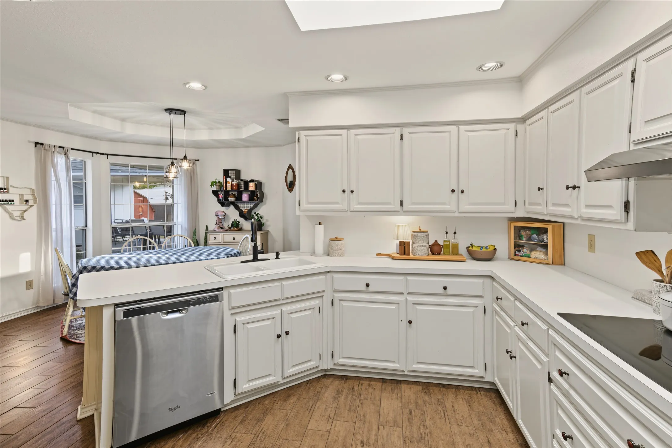 White cabinetry with black hardware, stainless steel dishwasher, integrated sink, electric cooktop, and wood-finish flooring