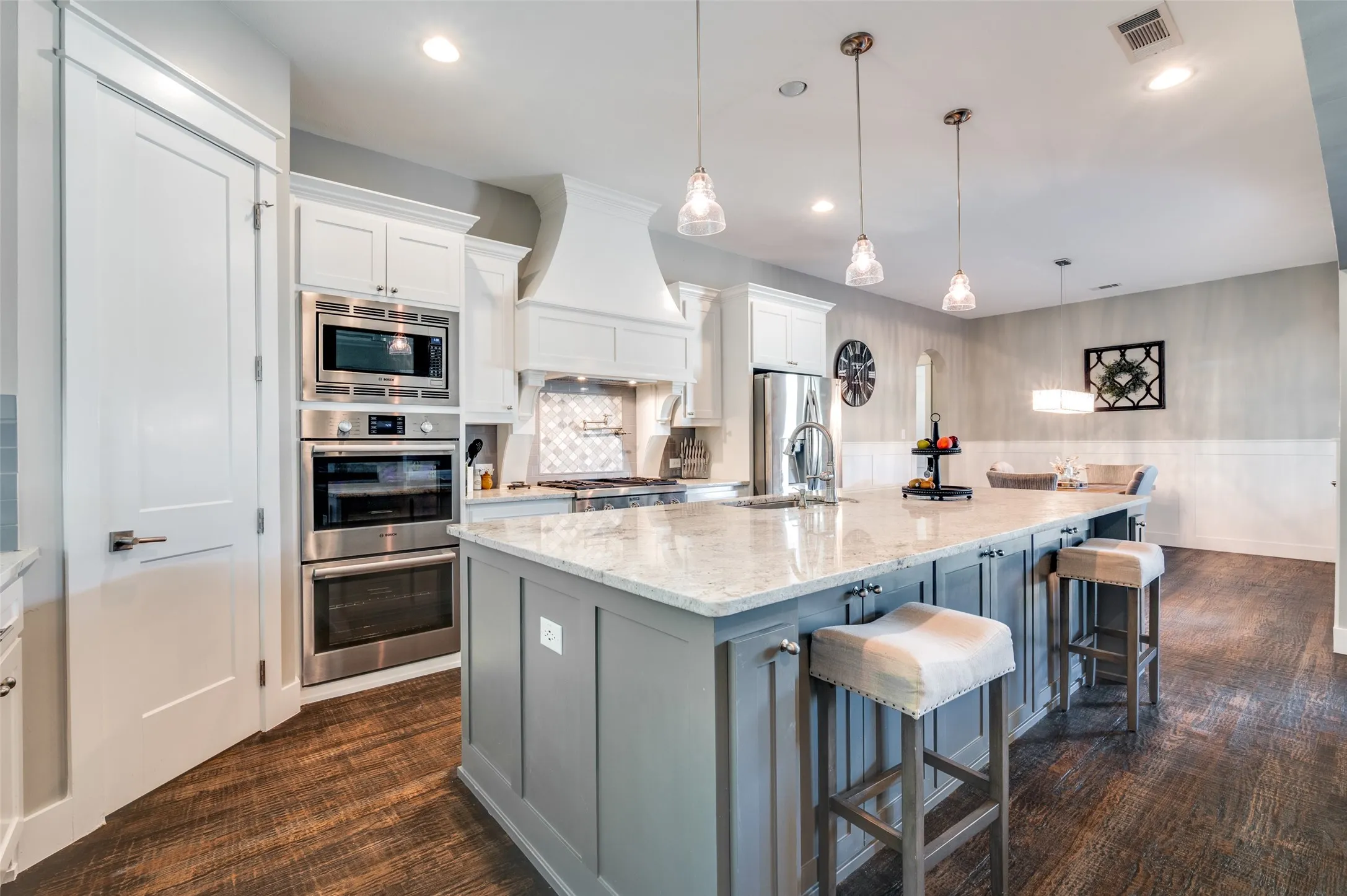 Kitchen featuring a large island with a stone countertop, built-in stainless steel appliances, pendant lighting, and wood-finish flooring