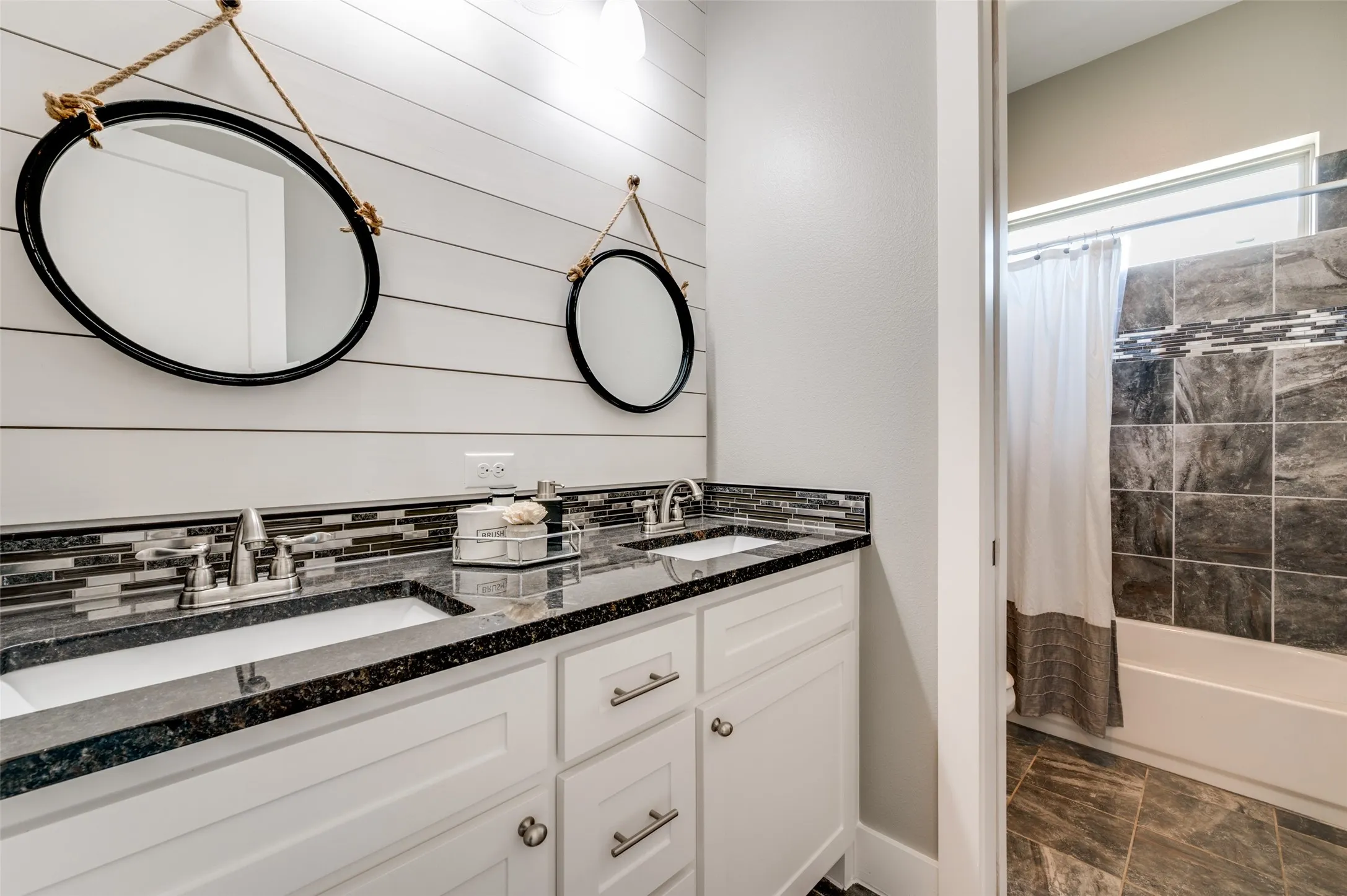 Dual vanity with white shaker-style cabinetry, dark speckled countertop, and subway tile backsplash