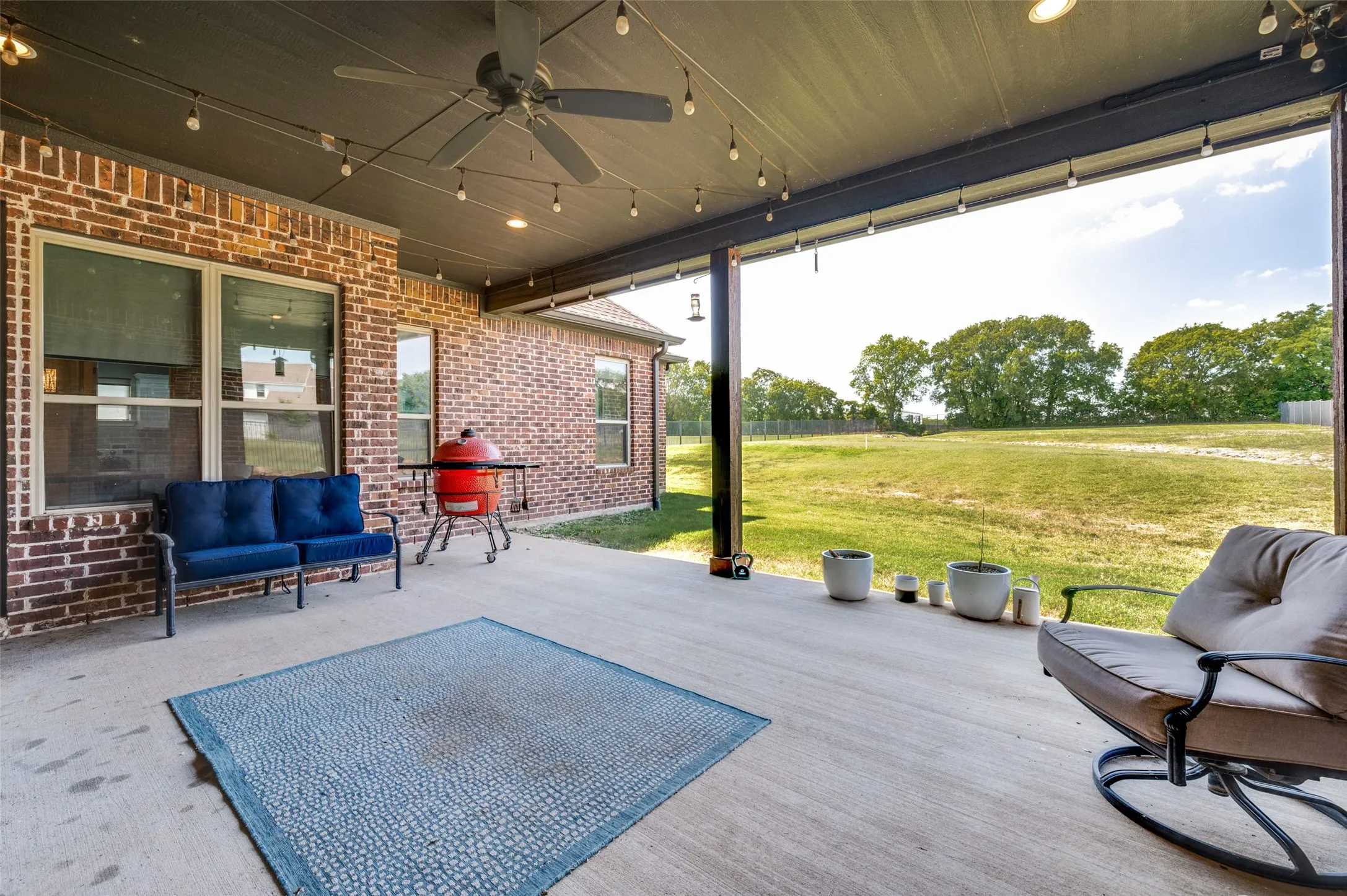 Expansive covered patio with a ceiling fan, string lights, and concrete flooring, featuring a brick exterior
