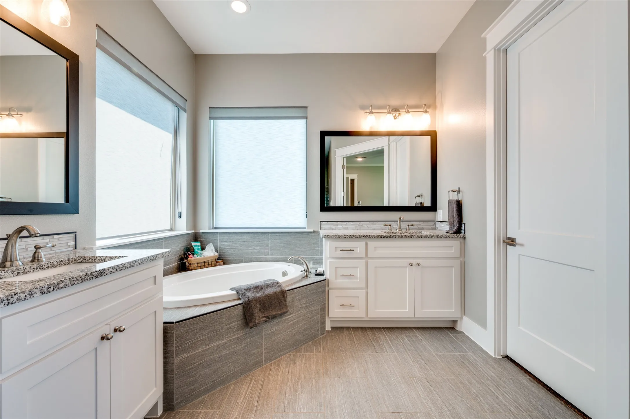 Dual vanity with light-colored countertops, a built-in bathtub with tiled surround, and wood-finish floor tiling