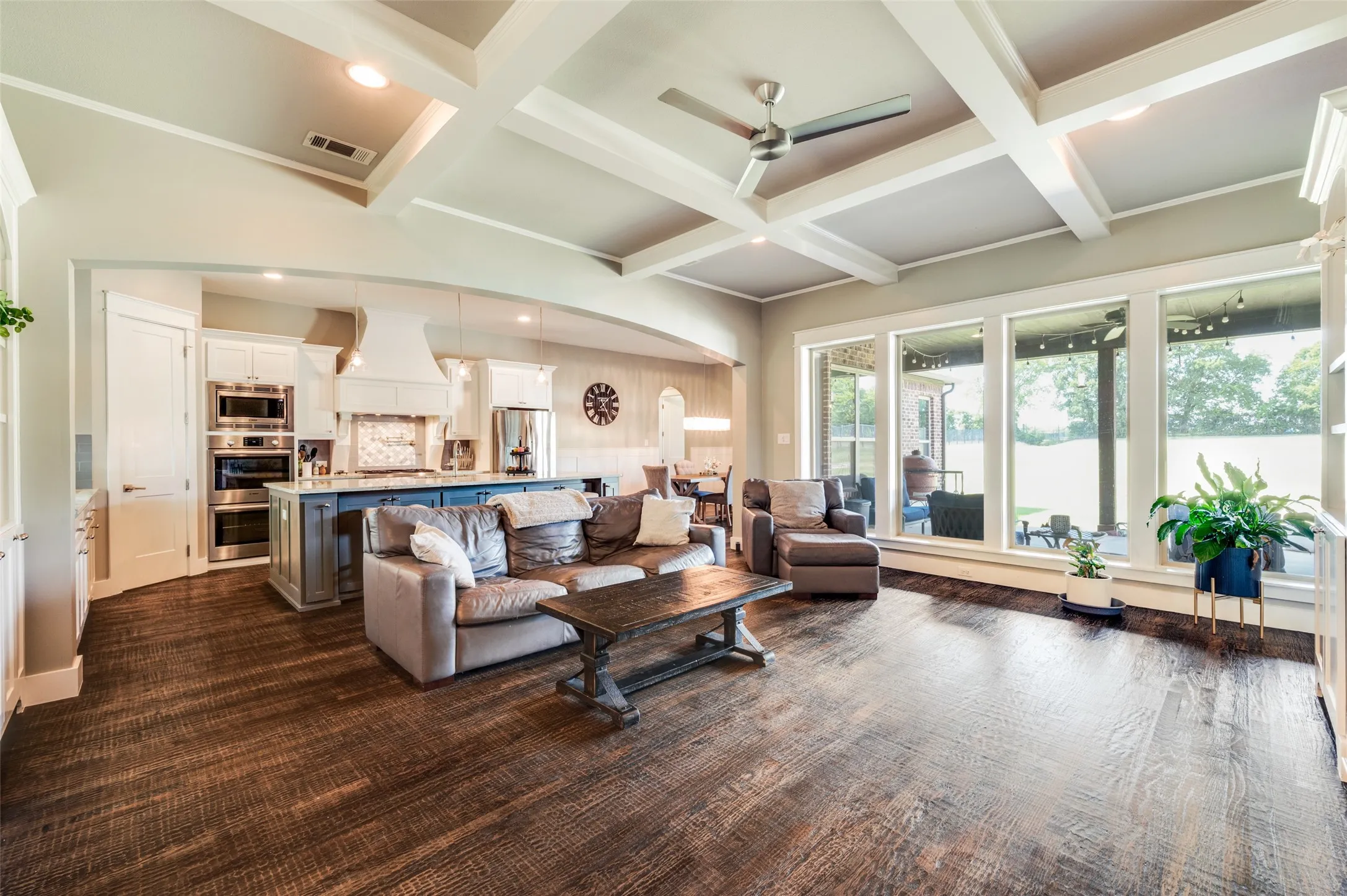 Spacious open-concept living area featuring high coffered ceilings, wood-finish flooring, and large picture windows