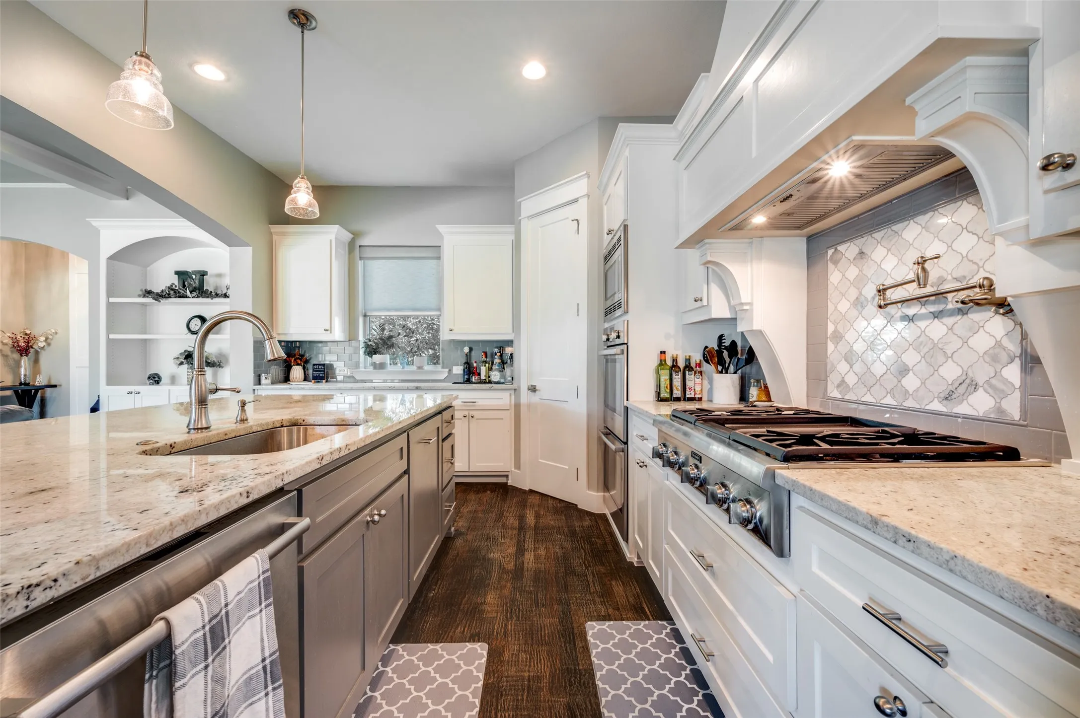 Gourmet kitchen featuring a large island with an undermount sink, granite countertops, wood-finish flooring, a commercial-style range with a pot filler, and a decorative range hood