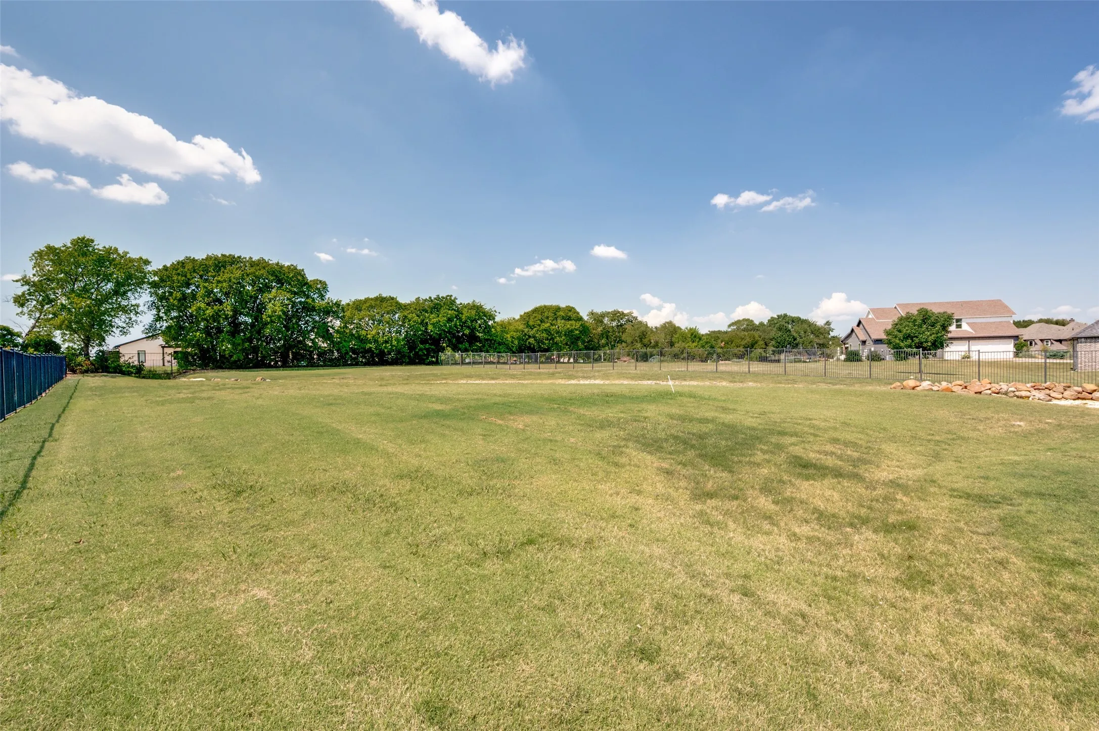 Expansive lot with lush green lawn, full perimeter fencing, and mature trees along the boundary