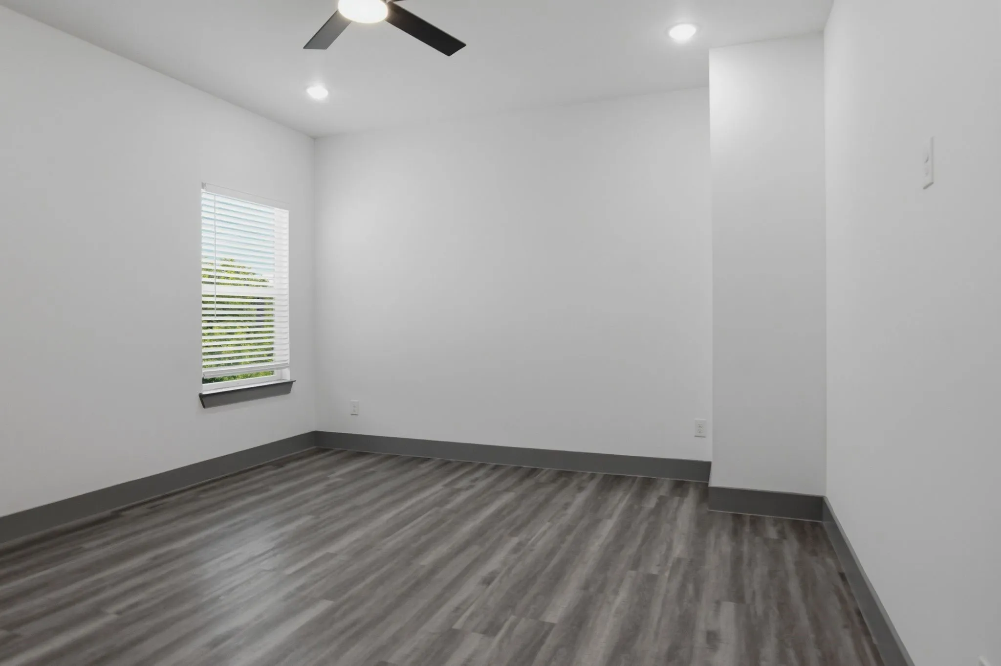 Wood-finish flooring, recessed lighting, ceiling fan, window with blinds, and contrasting baseboards
