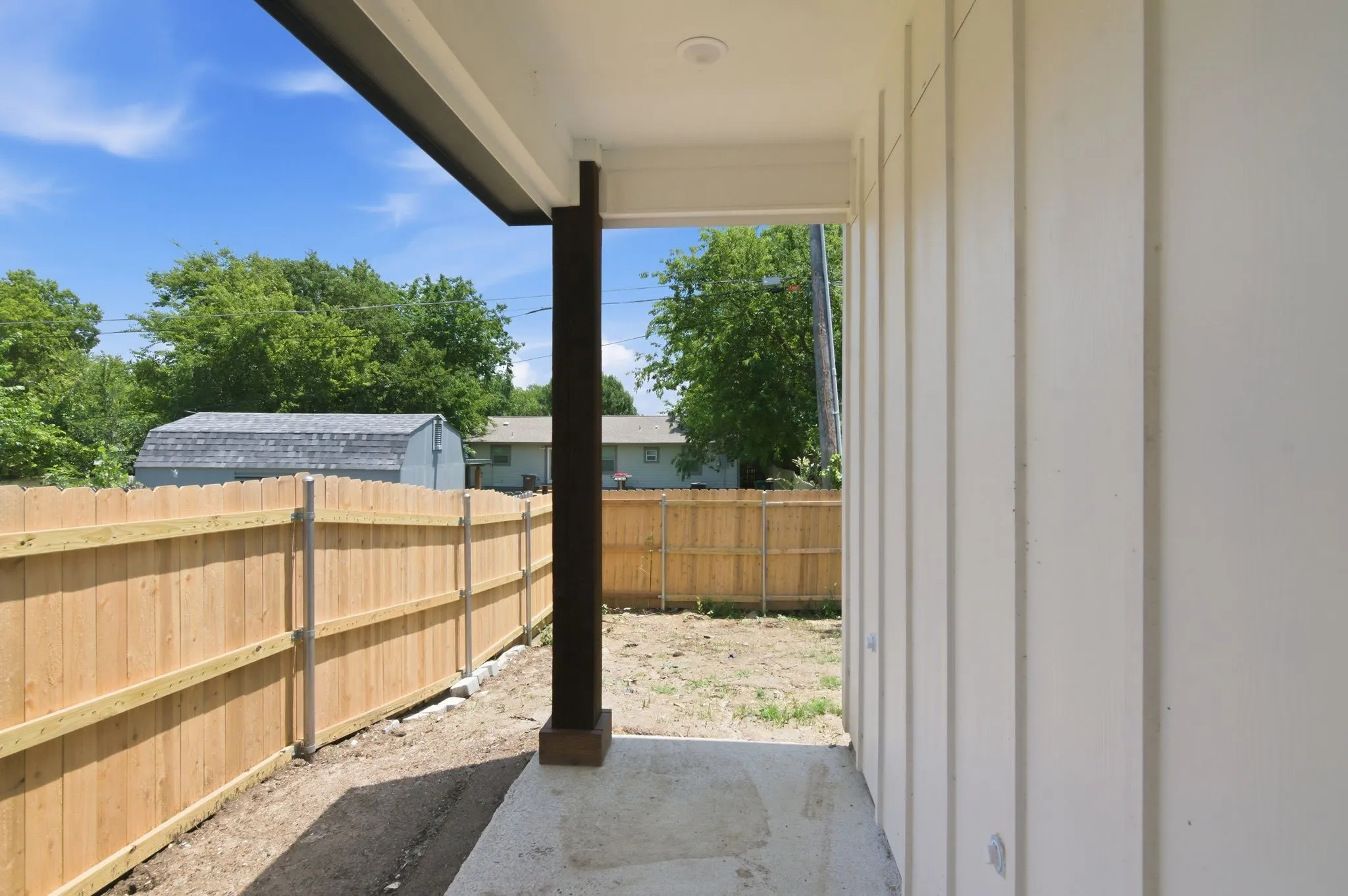 Covered patio featuring a concrete slab and wood-paneled walls, bordered by a wood fence