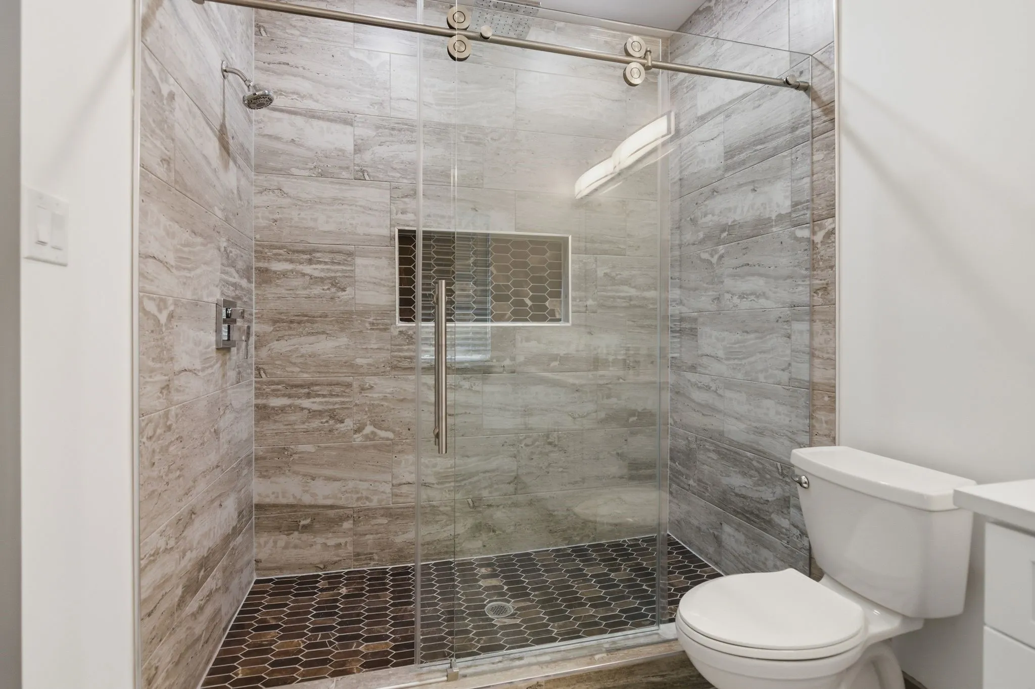 Walk-in shower with full-height tile surround, glass sliding door, and hexagonal tile flooring
