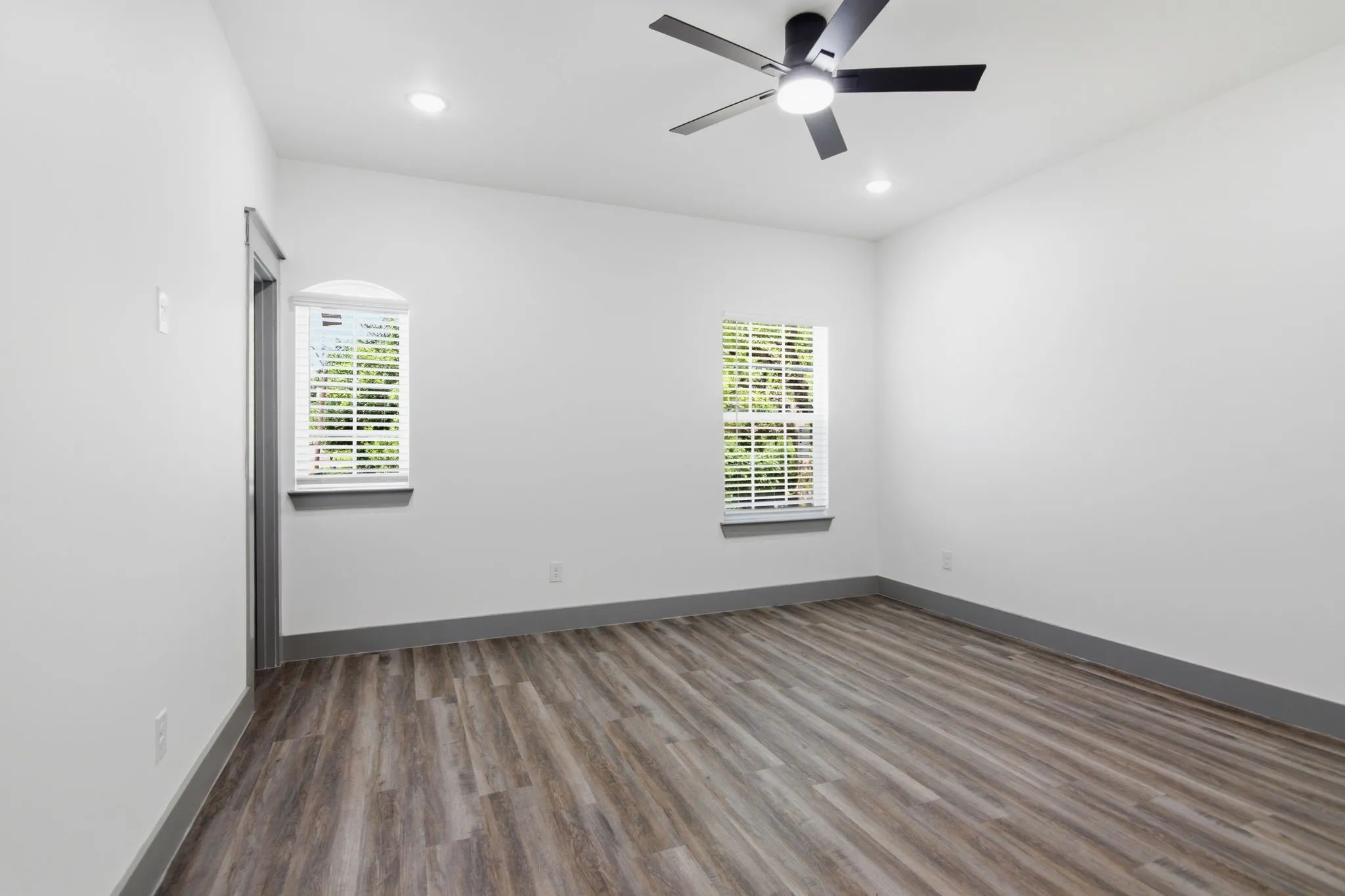 Wood-finish flooring, recessed lighting, ceiling fan, two windows with blinds, and contrasting trim