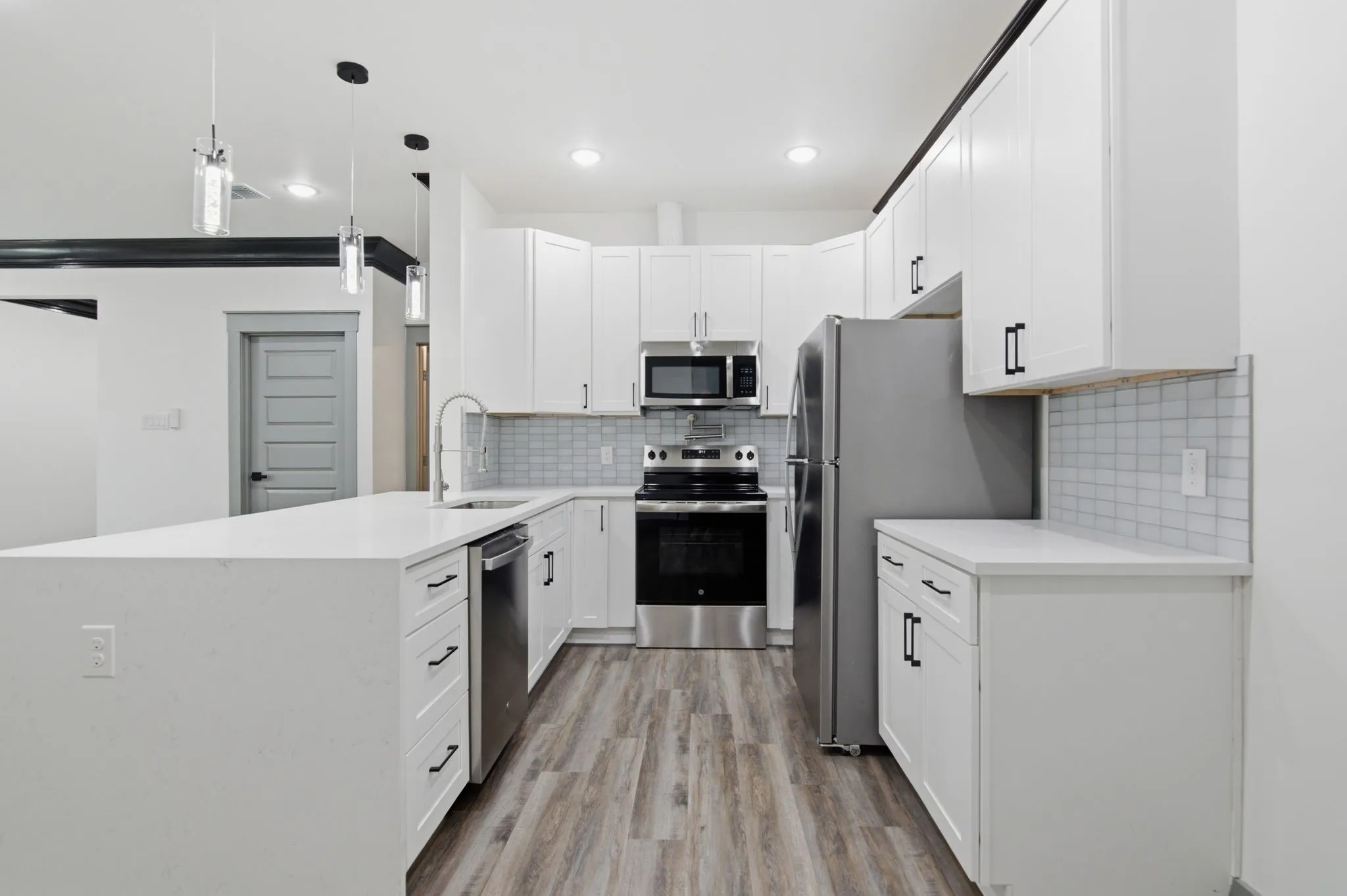 White cabinetry with black hardware, stainless steel appliances, wood-finish flooring, light-toned backsplash, and recessed lighting