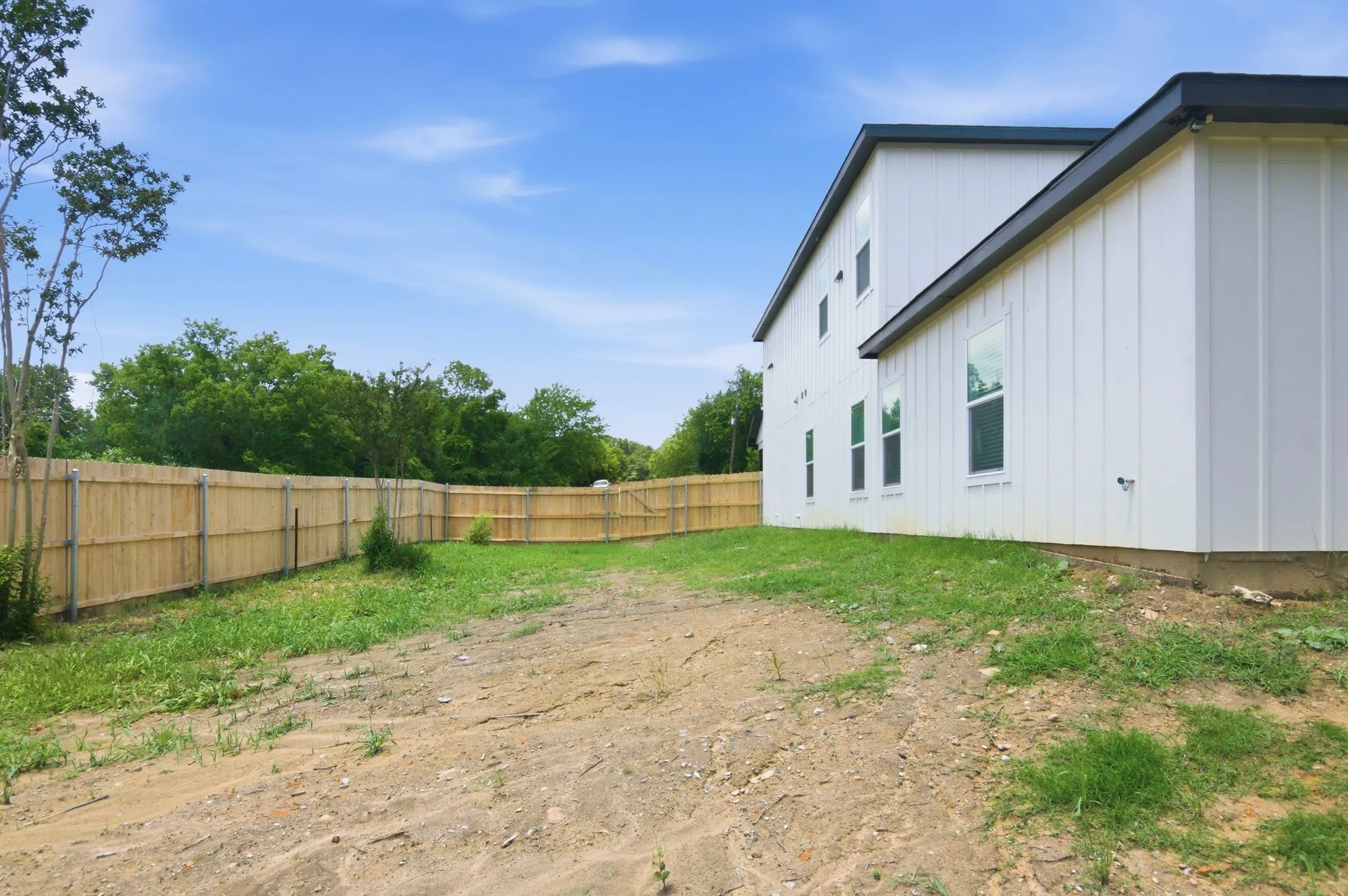 Two-story exterior with vertical white siding, multiple windows, and a dark roofline, featuring a wood privacy fence defining the property perimeter