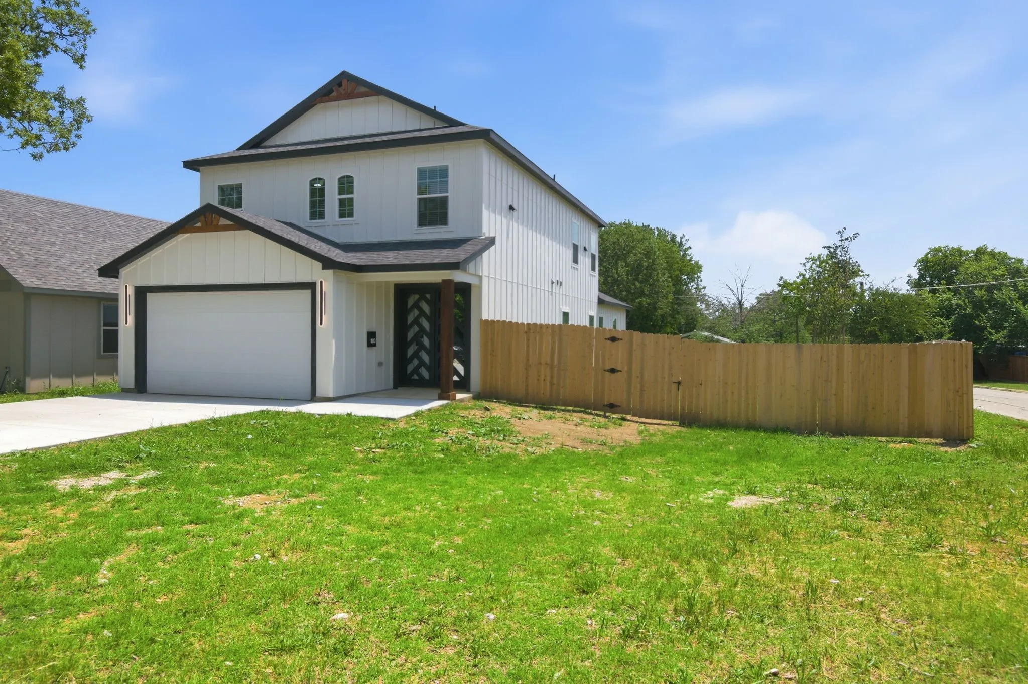 Two-story exterior with white vertical siding, black trim accents, a single-car garage, and a wood privacy fence