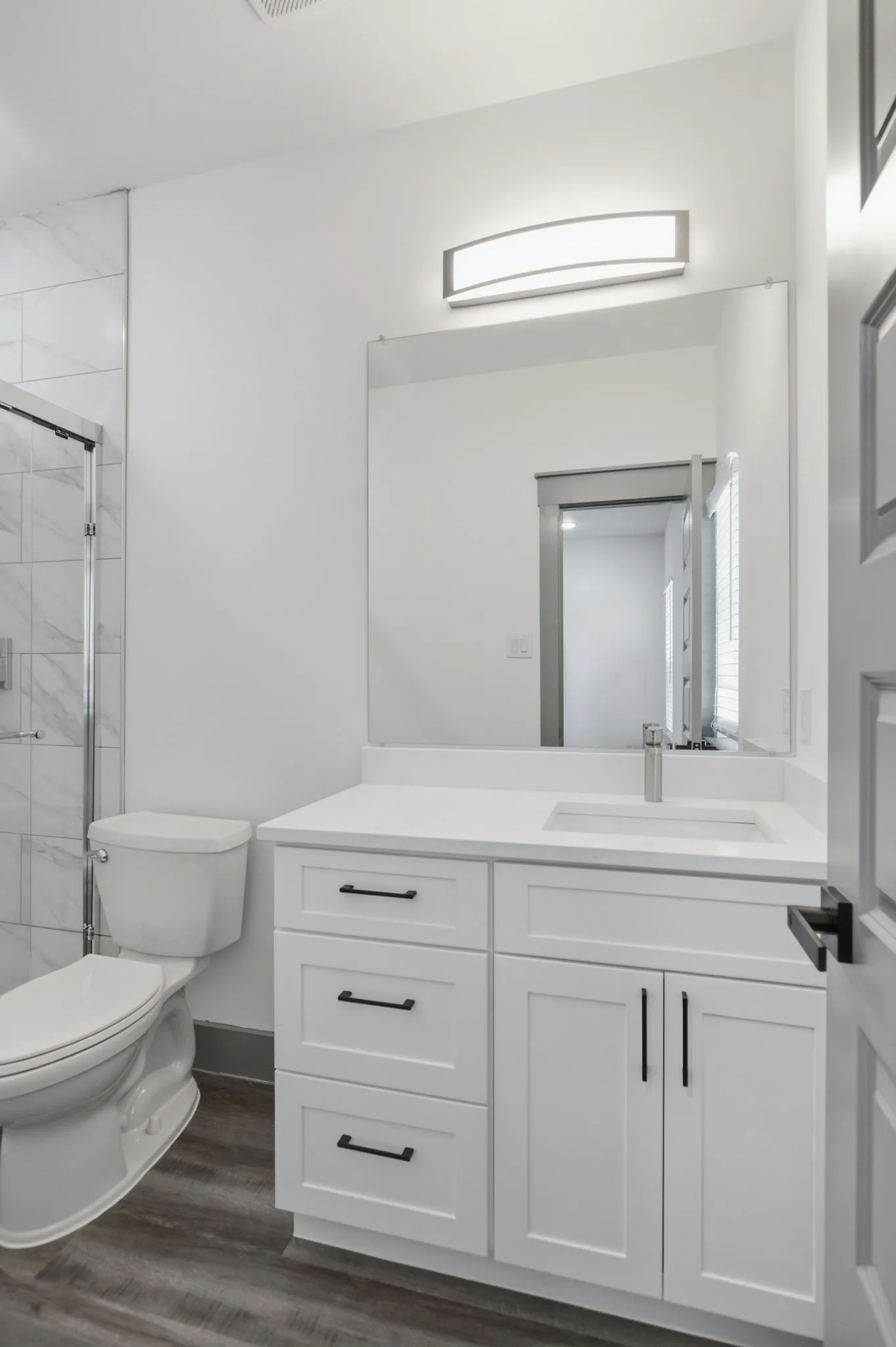 White vanity with black hardware, white countertop, integrated sink, and a framed mirror