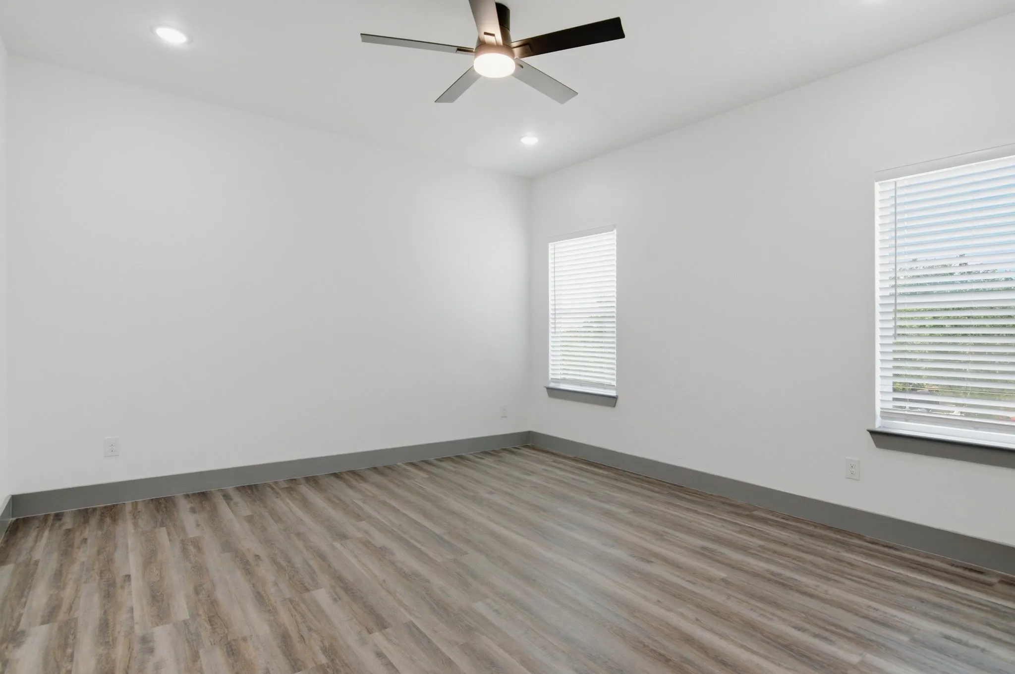 Recessed ceiling lighting, modern ceiling fan, two windows with blinds, and wood-finish flooring