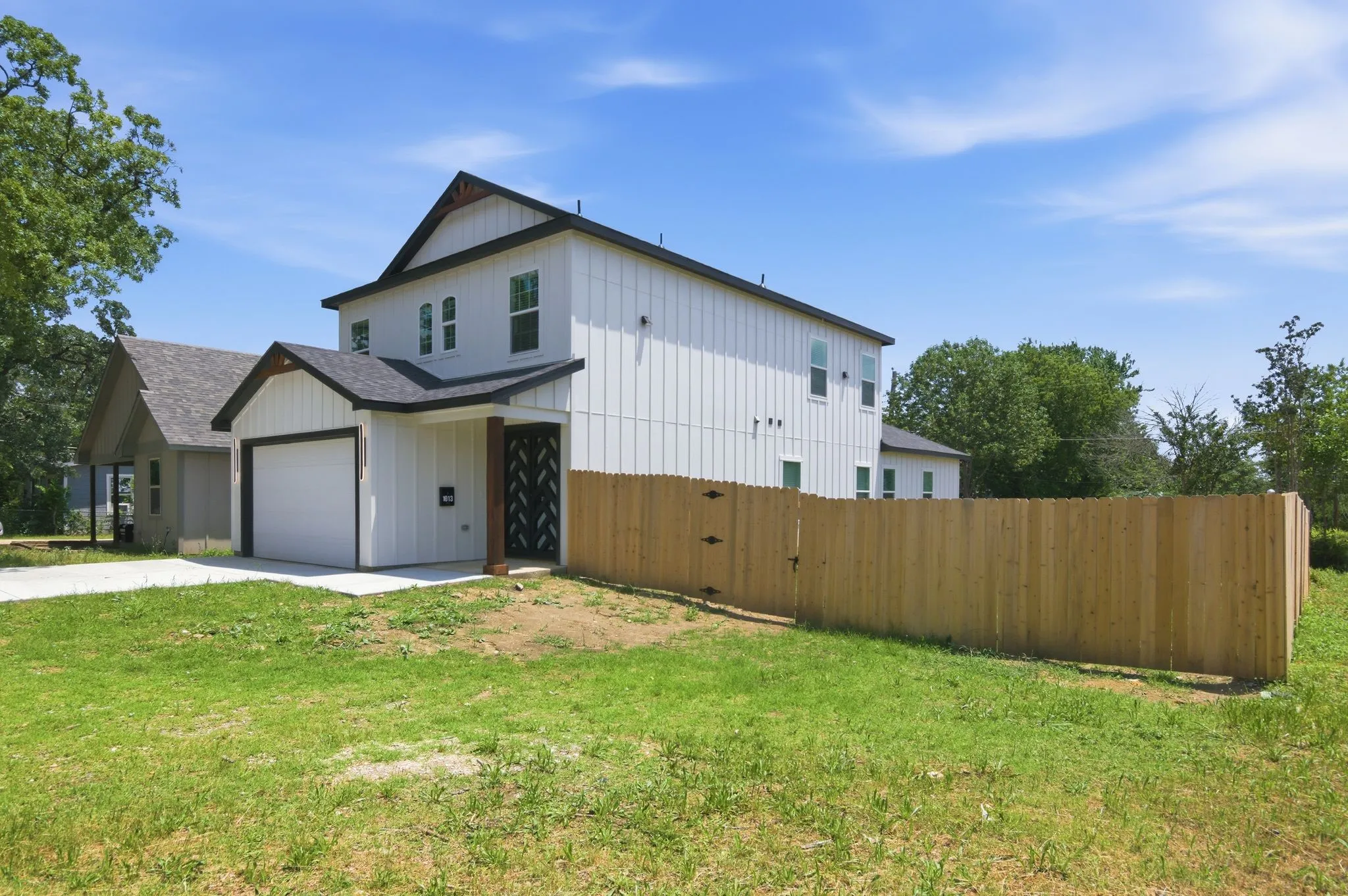 Two-story vertical siding exterior, attached garage, covered entryway with wood-tone support beam, dark-framed windows, and private wooden fencing