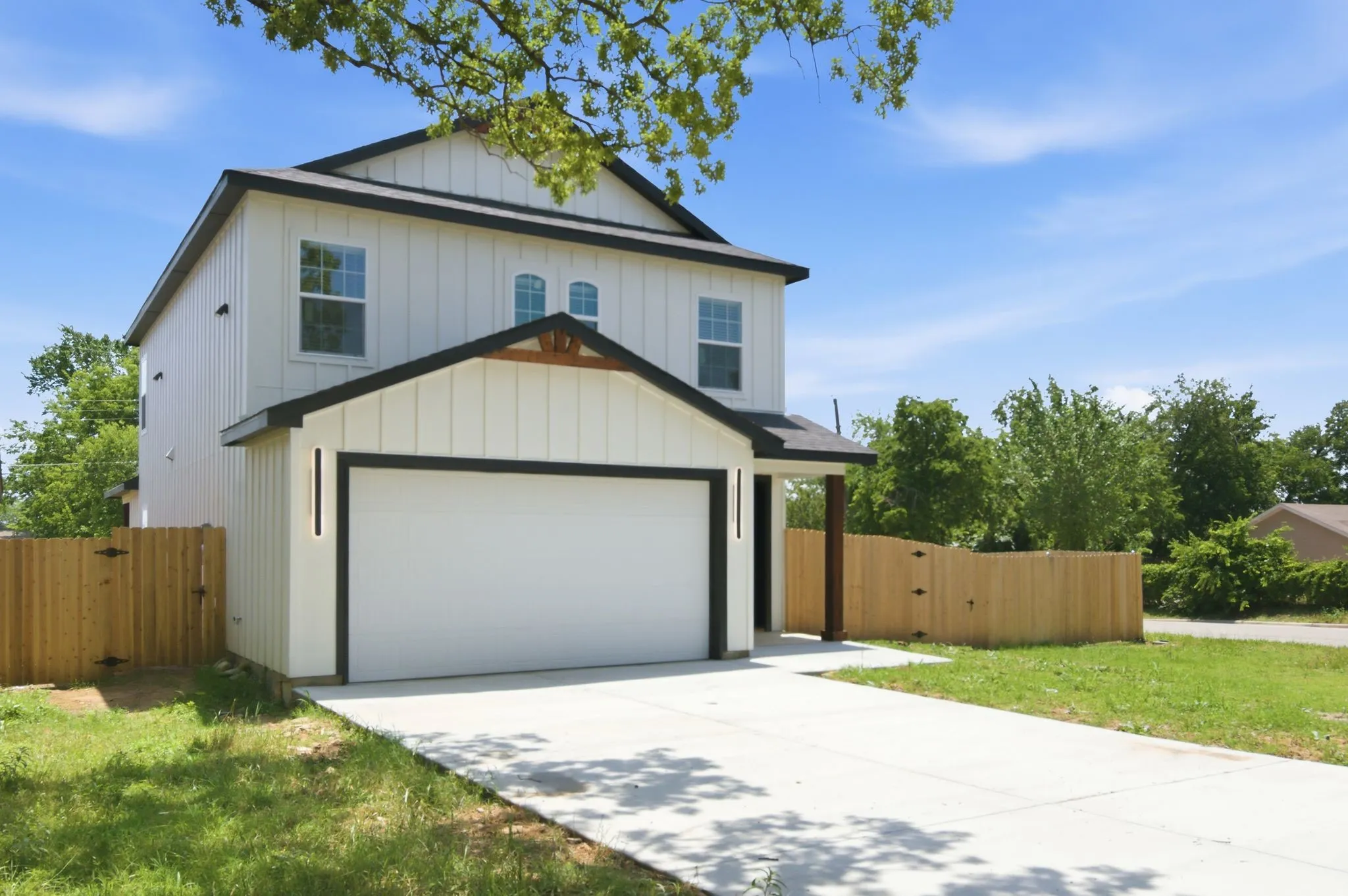 Two-story residence featuring vertical panel siding, dark trim accents, a two-car garage, and a wood privacy fence