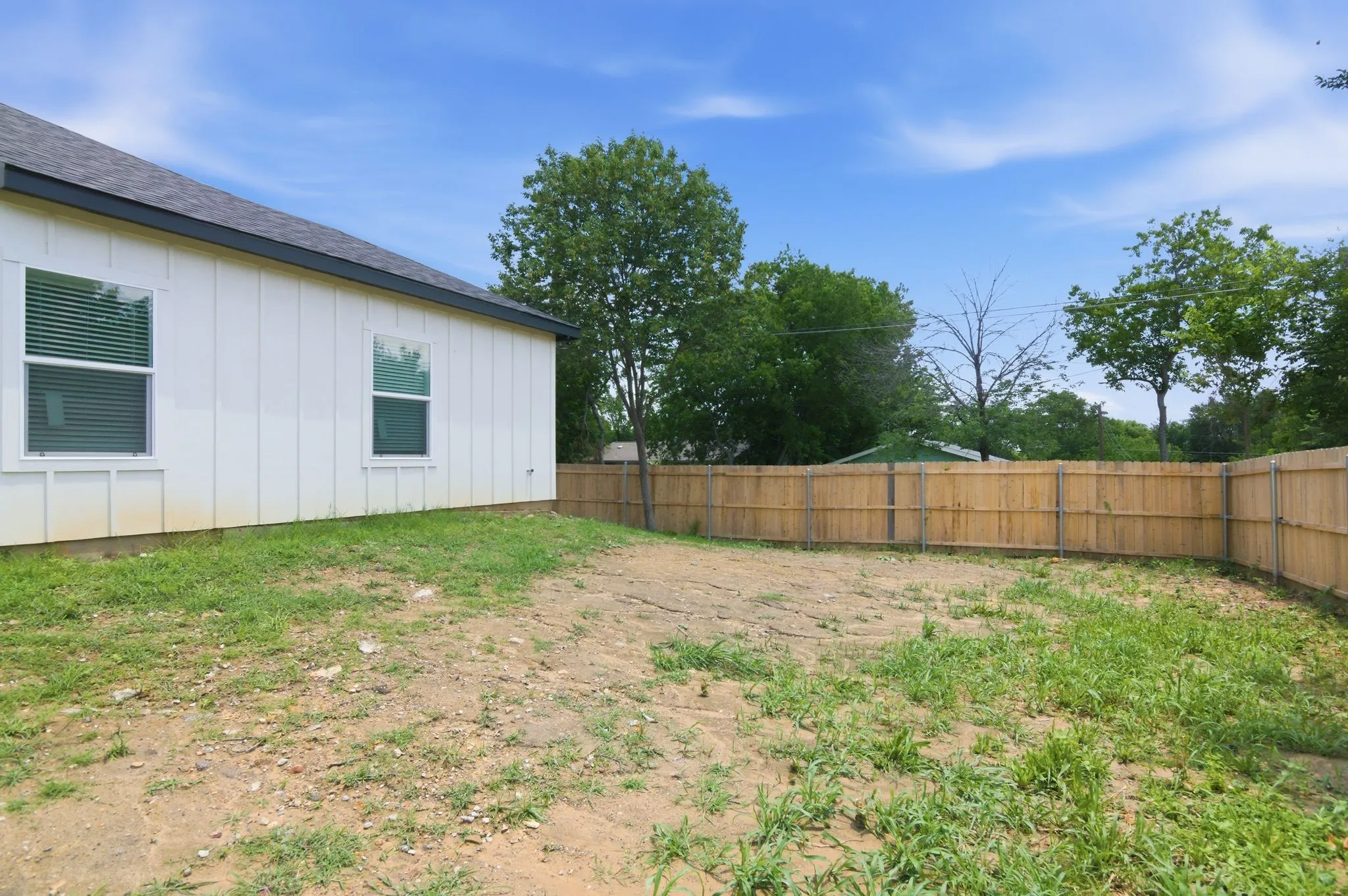 White vertical siding, dark roofline, wood privacy fencing, and a grassy area