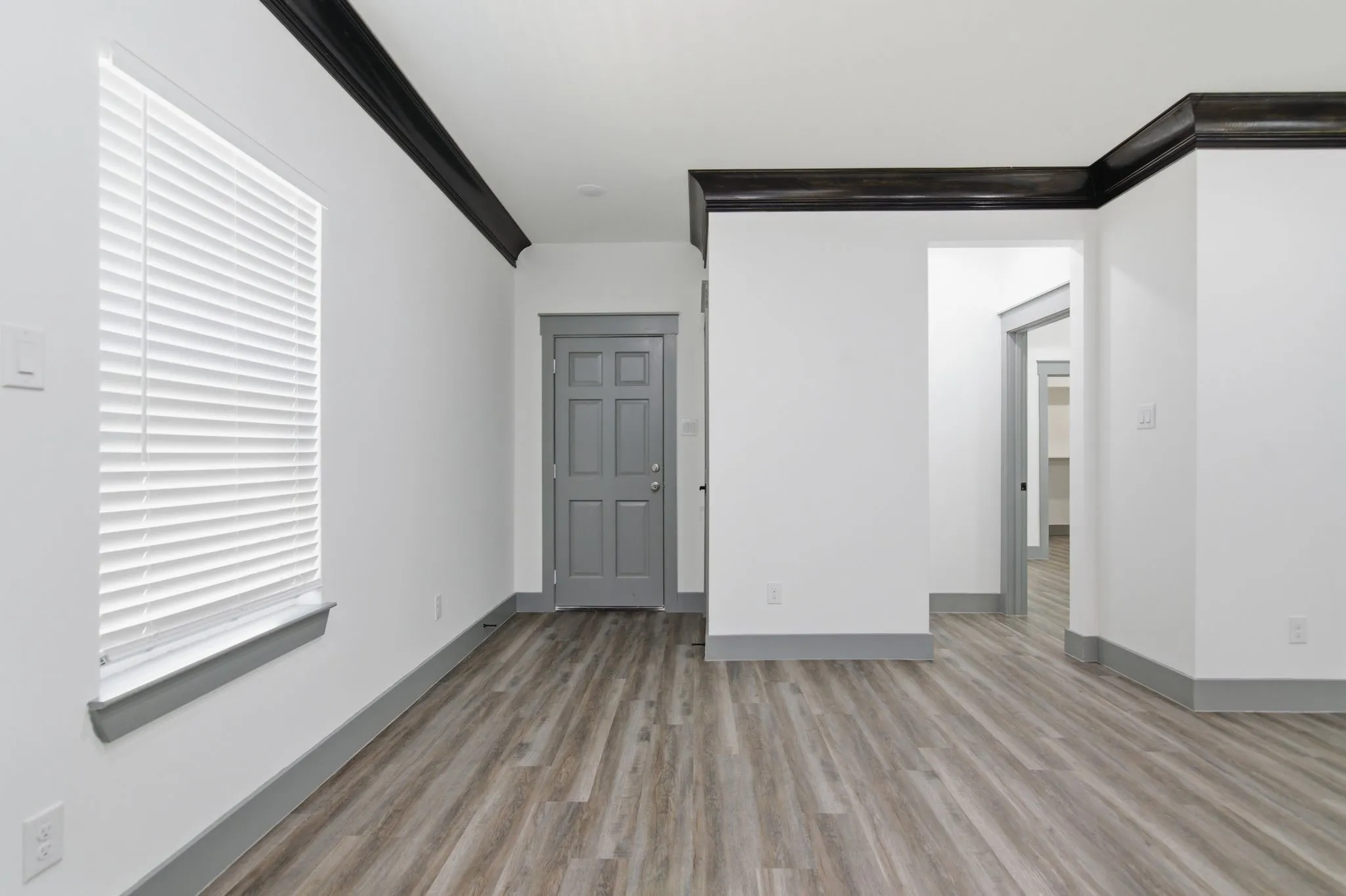 Wood-finish flooring, white walls, dark crown molding, gray trim, and a paneled door