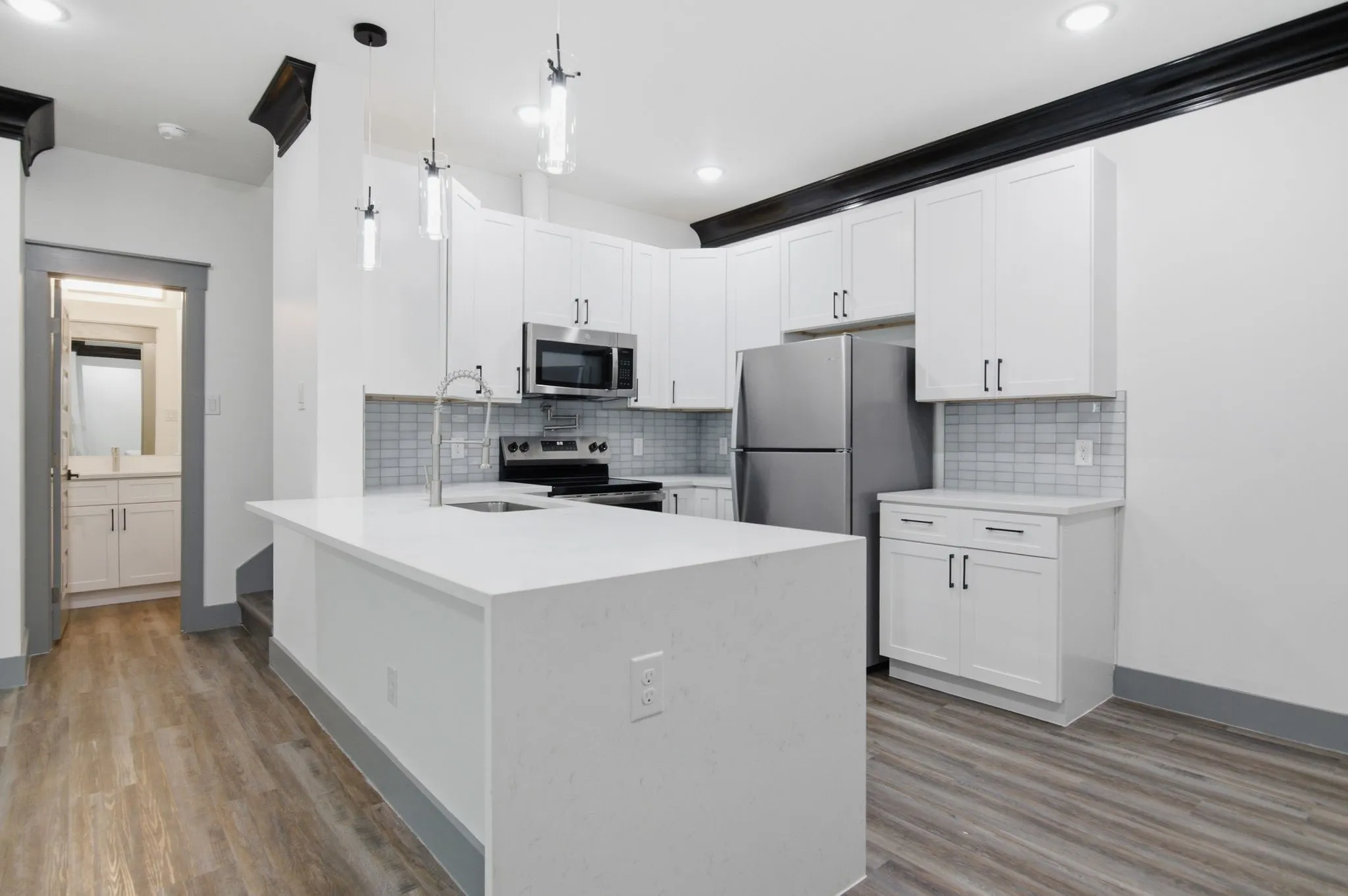 Kitchen featuring white cabinetry, stainless steel appliances, a center island with sink, subway tile backsplash, and wood-finish flooring