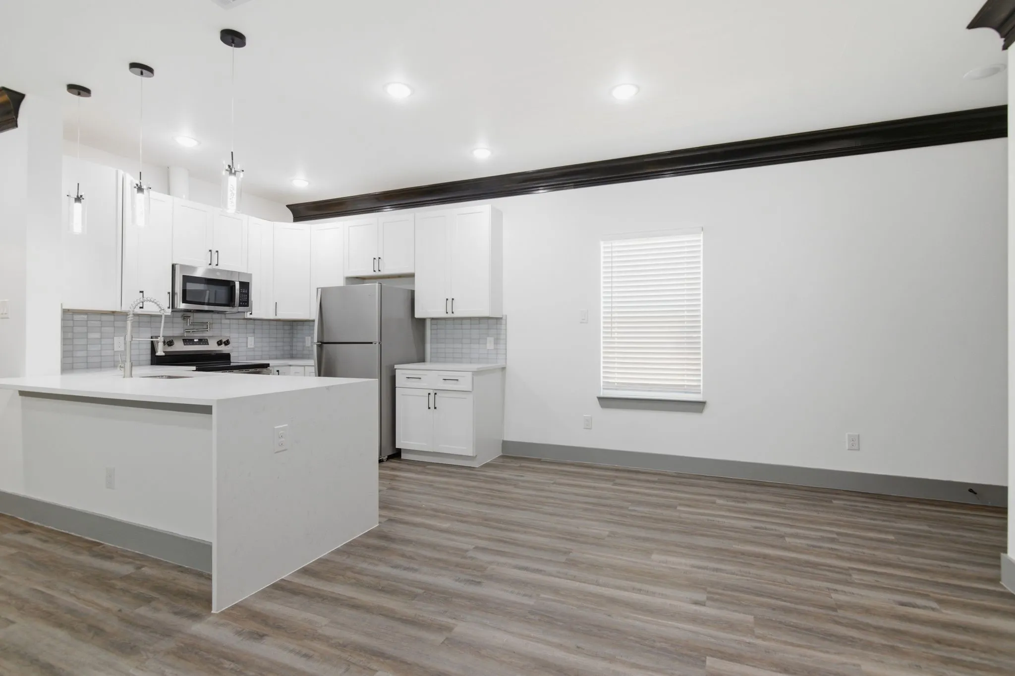 Kitchen featuring white cabinetry, stainless steel appliances, a center island with a sink, and wood-finish flooring
