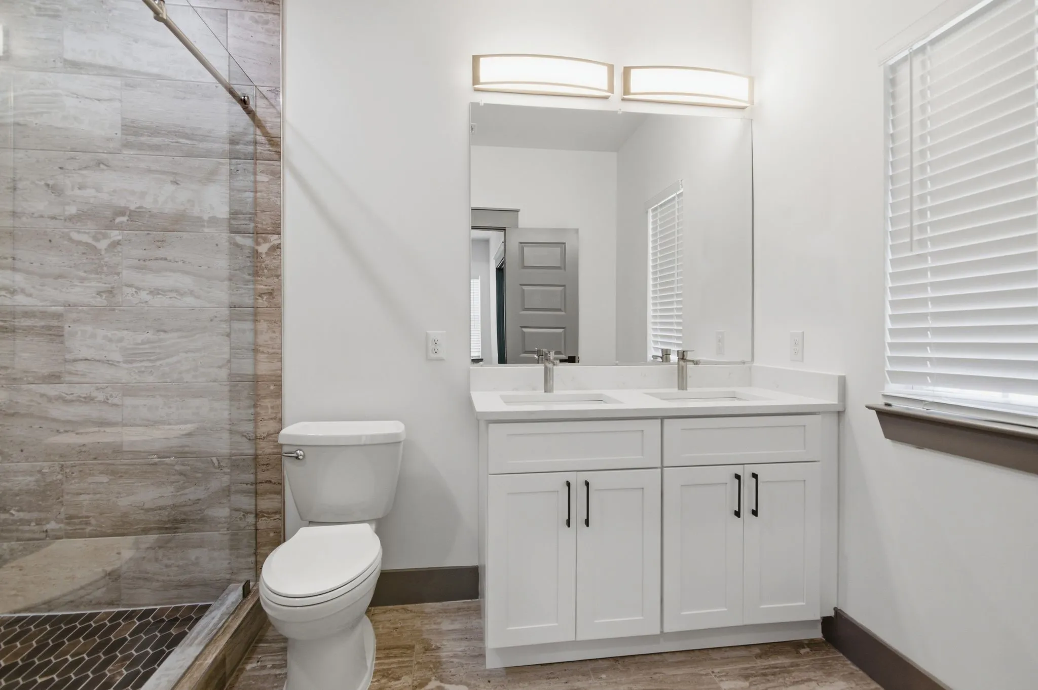 Dual vanity with white cabinetry, a large frameless mirror, and overhead lighting fixtures