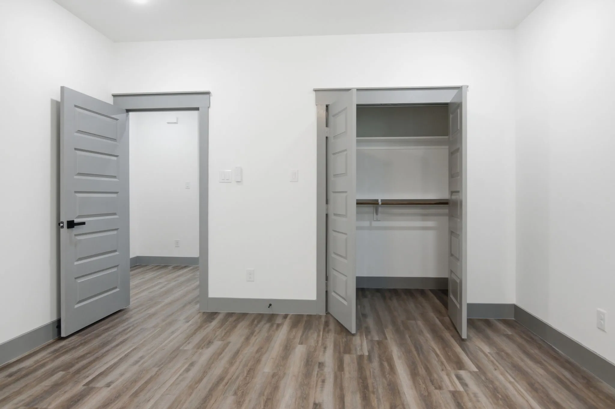 Wood-finish flooring throughout, bright white walls, recessed ceiling lighting, gray paneled doors with matte black hardware, and built-in closet shelving