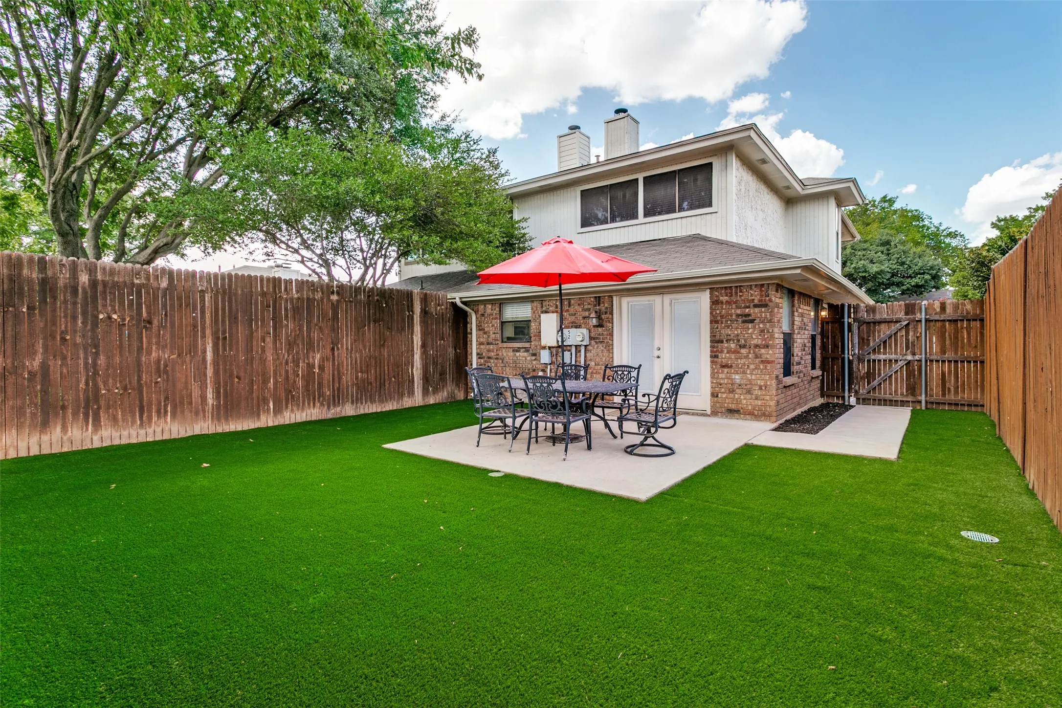 Expansive backyard featuring artificial turf, a concrete patio, and a wood privacy fence