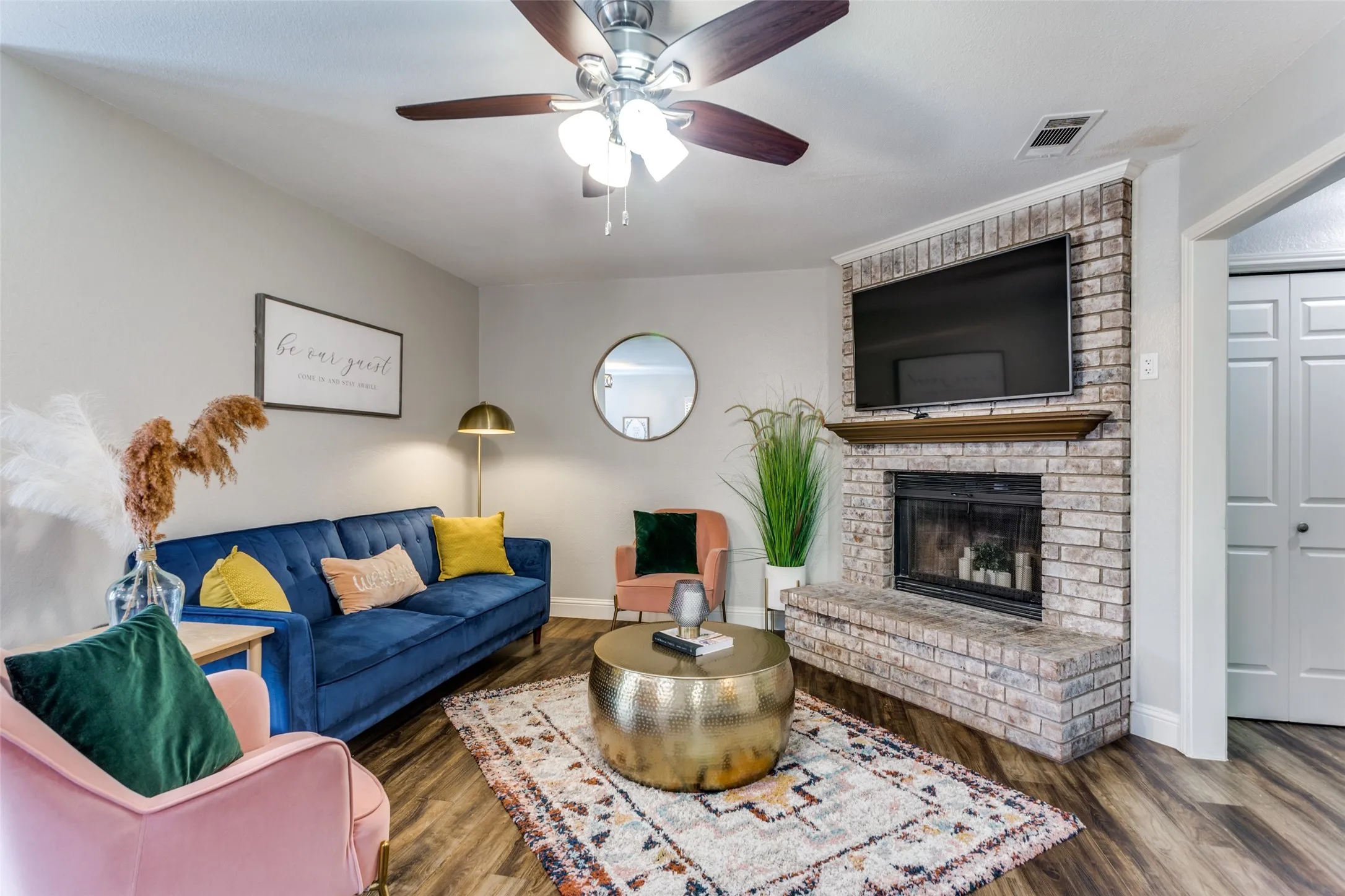 Living space featuring wood-finish flooring, a ceiling fan with integrated lighting, and a brick-faced fireplace with a wood mantel