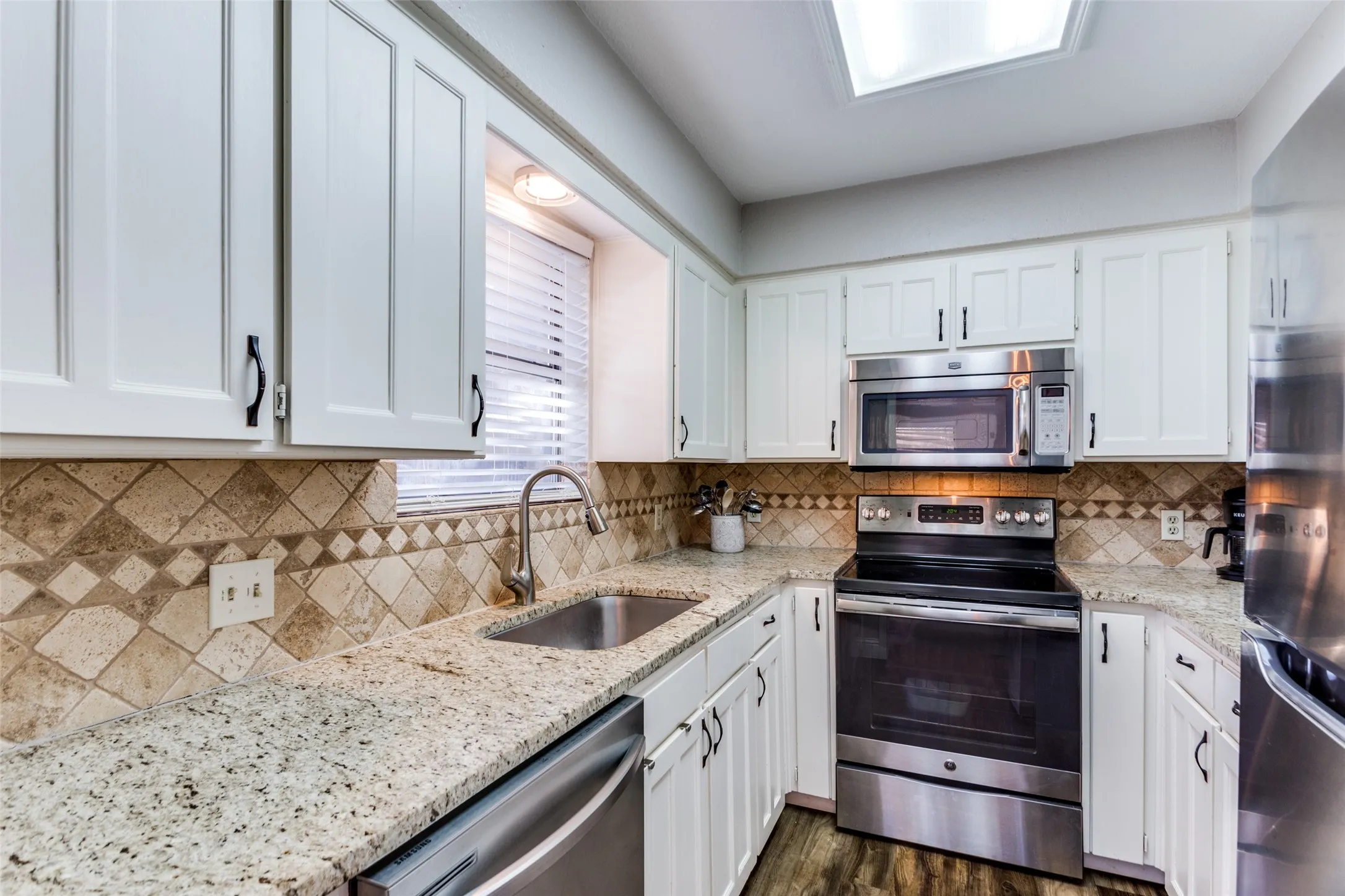 Kitchen featuring granite countertops, stainless steel appliances, white shaker cabinetry, tiled backsplash, and wood-finish flooring
