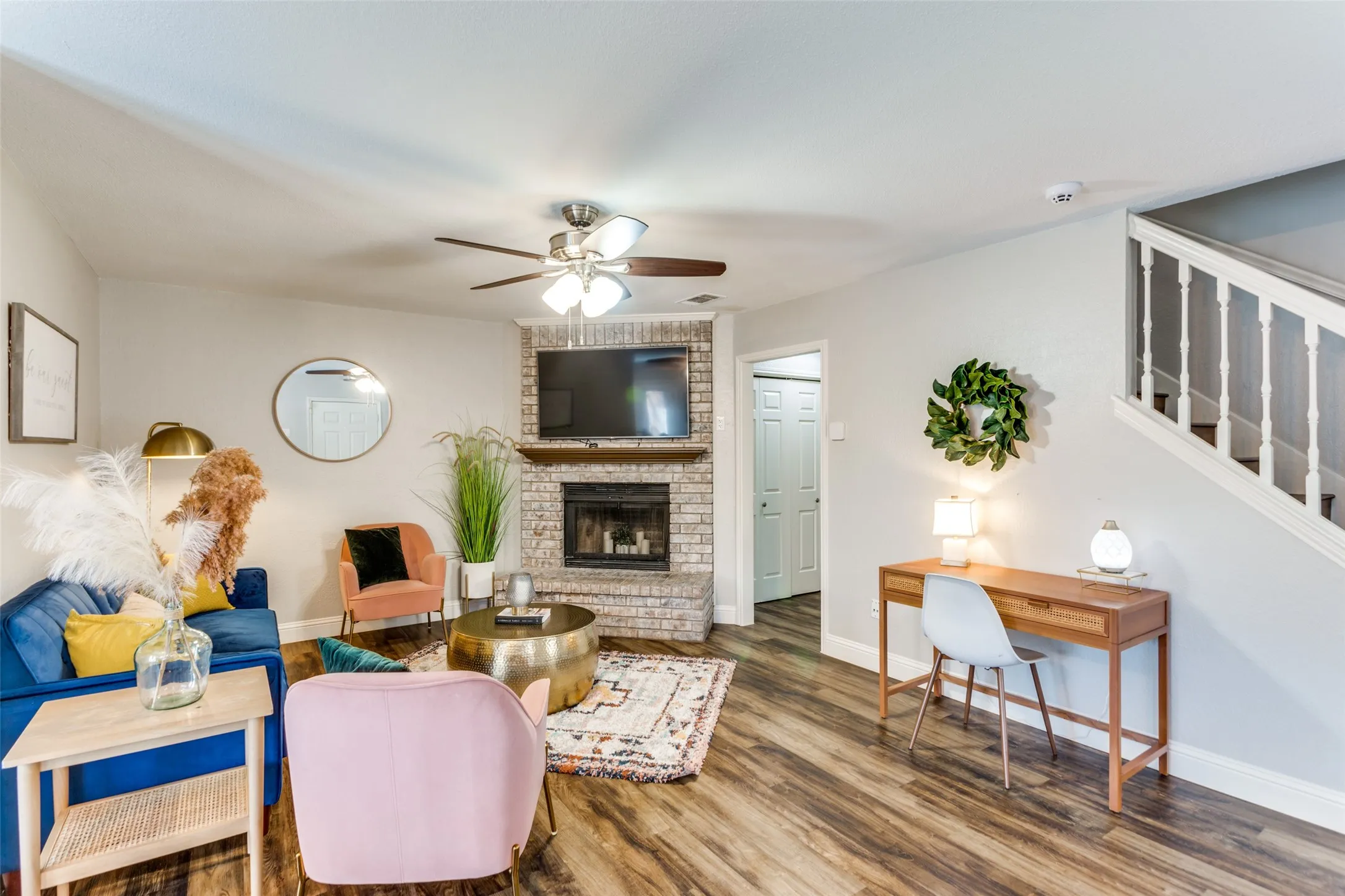 Warm living area featuring wood-finish flooring, a brick fireplace with a wood mantle, and a ceiling fan