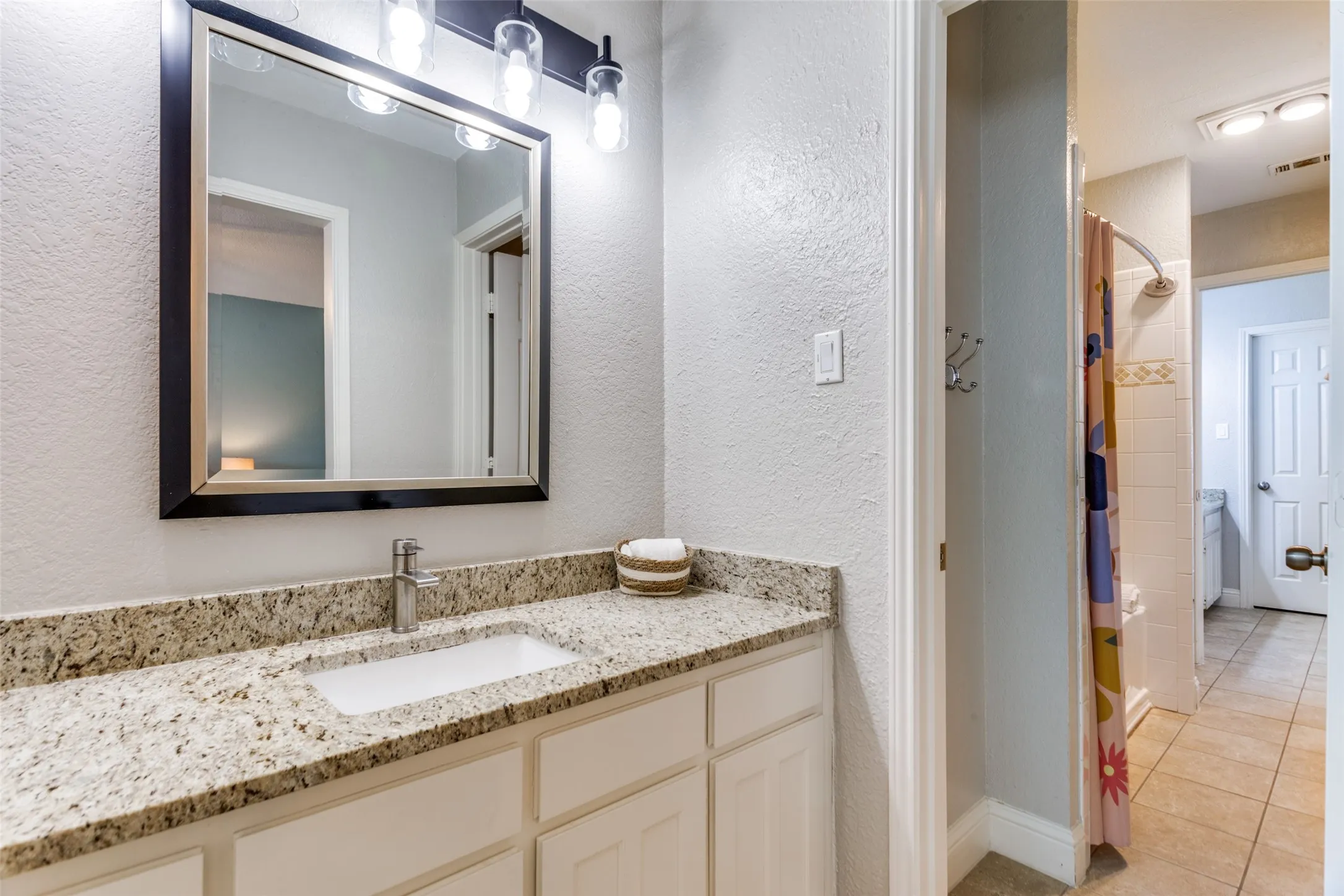 Bathroom featuring a single vanity with a granite countertop, undermount sink, and a framed mirror