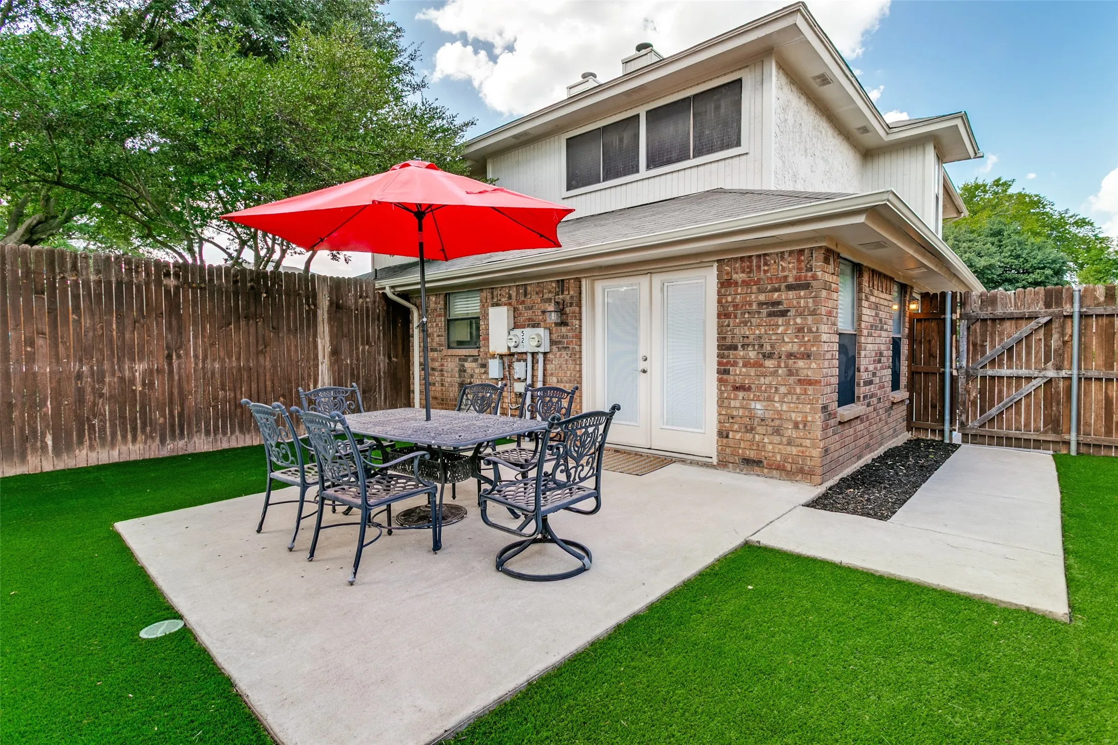 Private backyard featuring a concrete patio, artificial turf, wood fence, and brick exterior