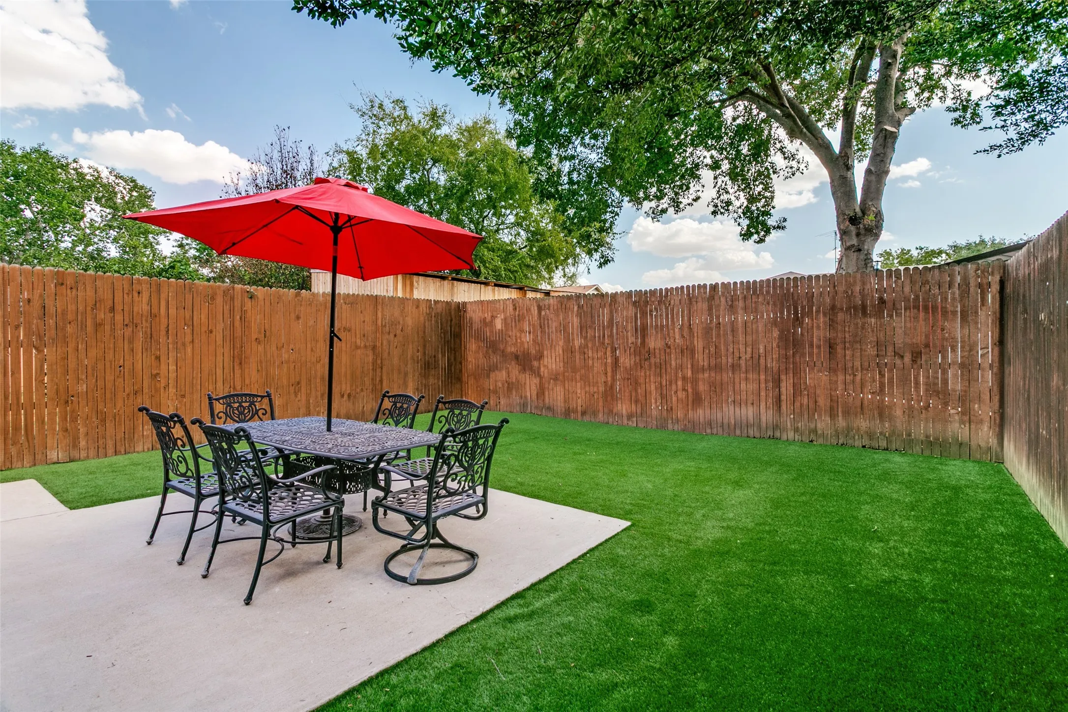 Private backyard featuring artificial turf, a concrete patio, and a wood fence enclosure