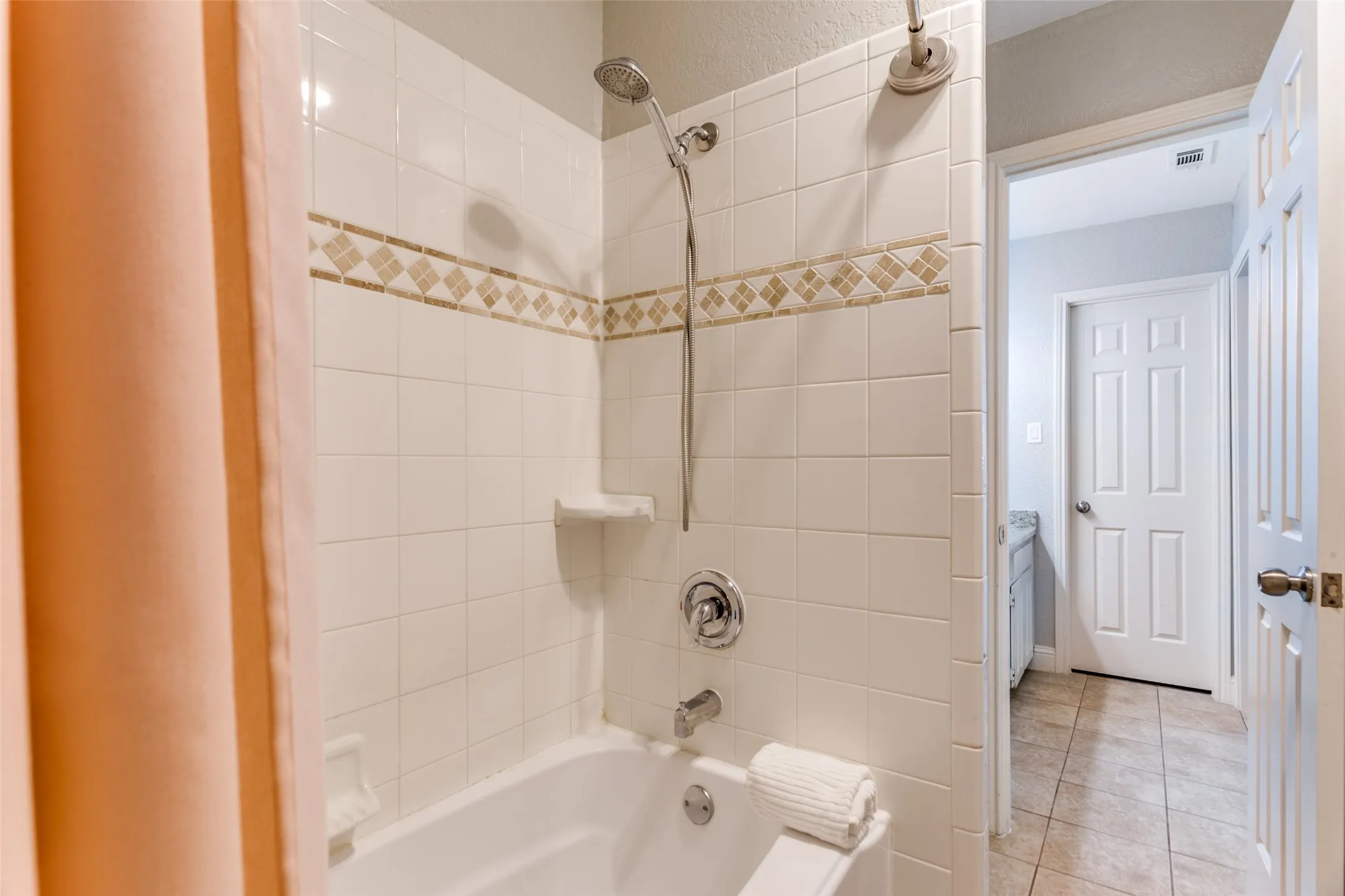 Bathtub and shower combination with white subway tile surround, decorative mosaic tile accent, and chrome fixtures