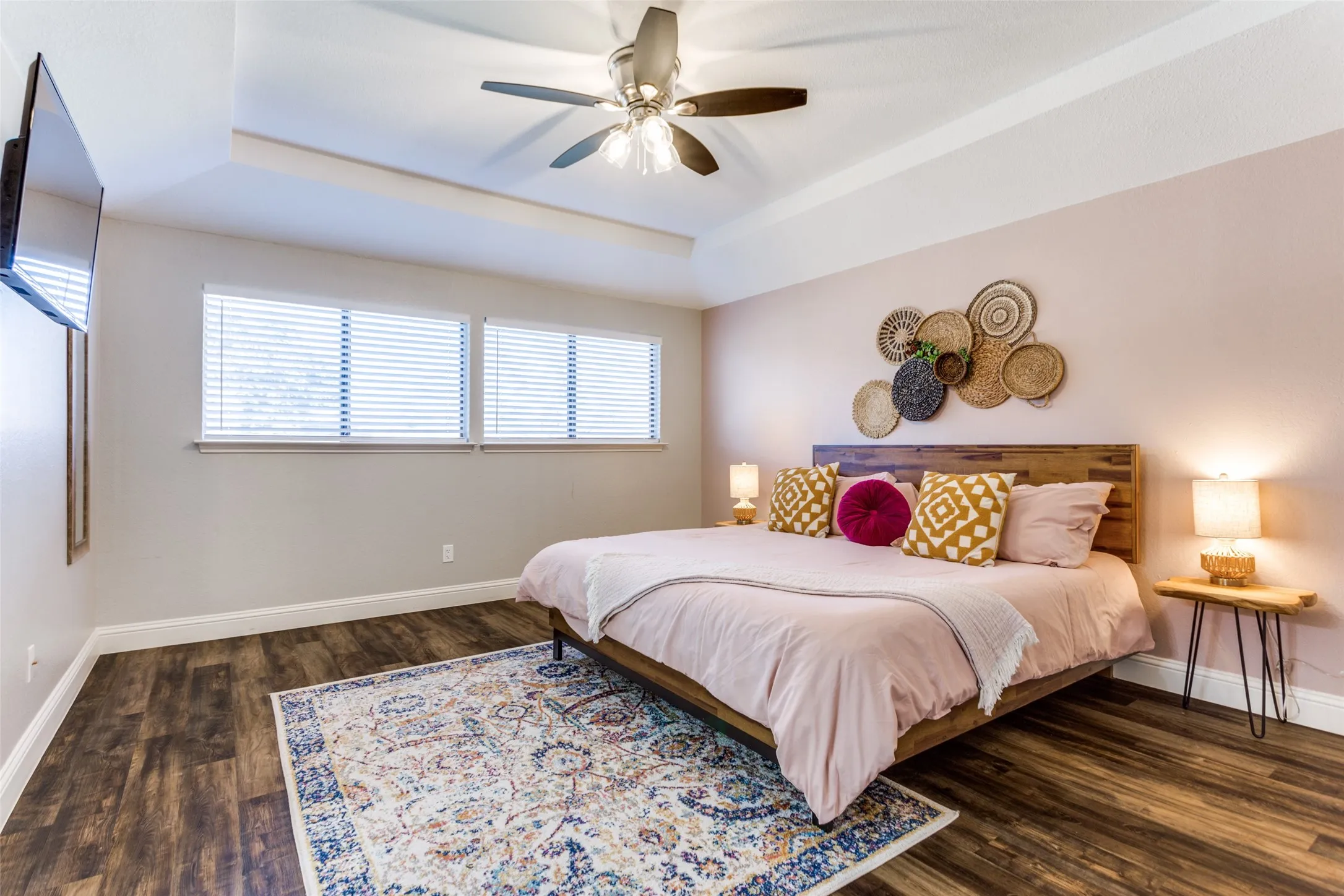 Tray ceiling with a ceiling fan, wood-finish flooring, and multiple windows with blinds