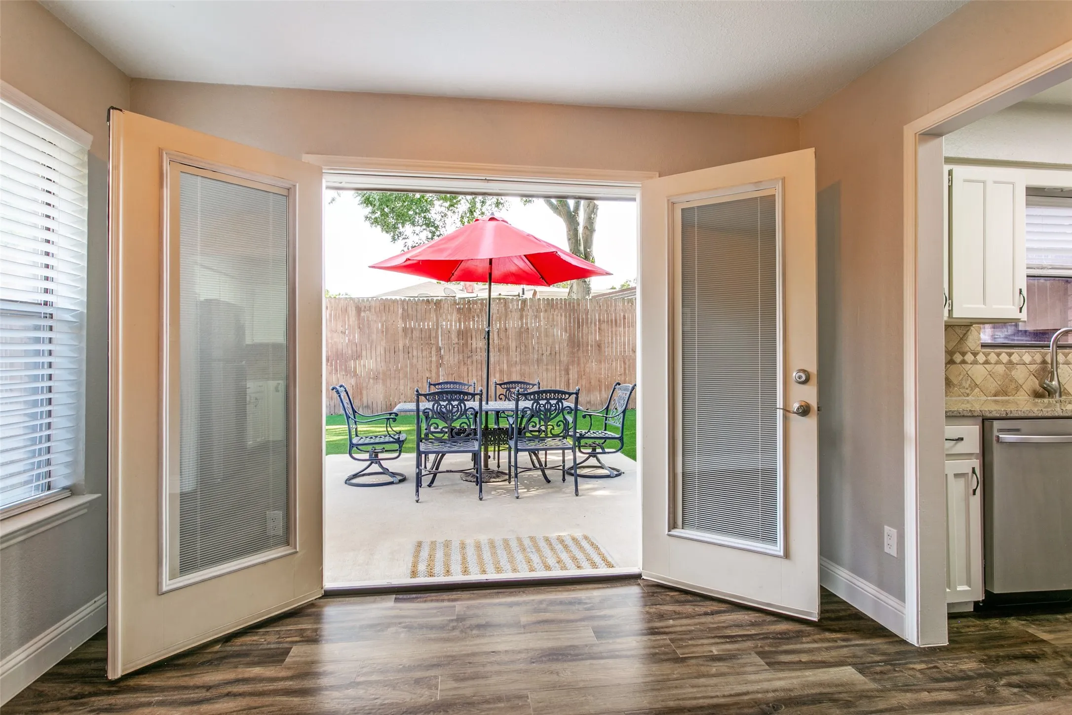 Wood-finish flooring, double glass-panel doors, concrete patio, fenced yard, and kitchen with stainless steel appliances