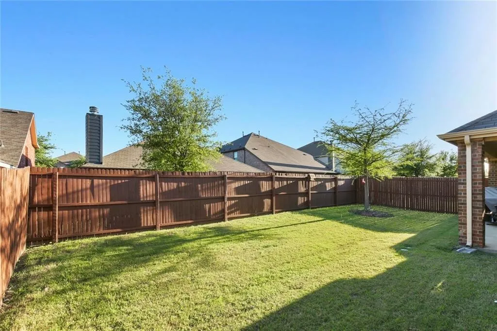 Expansive backyard featuring a manicured lawn, established trees, full wood privacy fencing, and a covered patio area with brick columns
