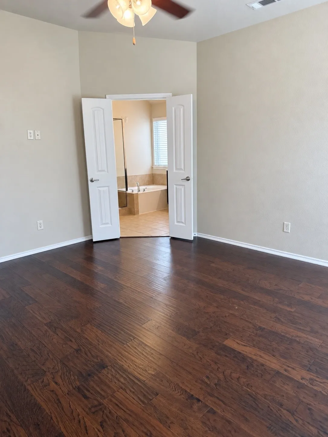Rich wood-finish flooring, ceiling fan with integrated lighting, and neutral wall tones