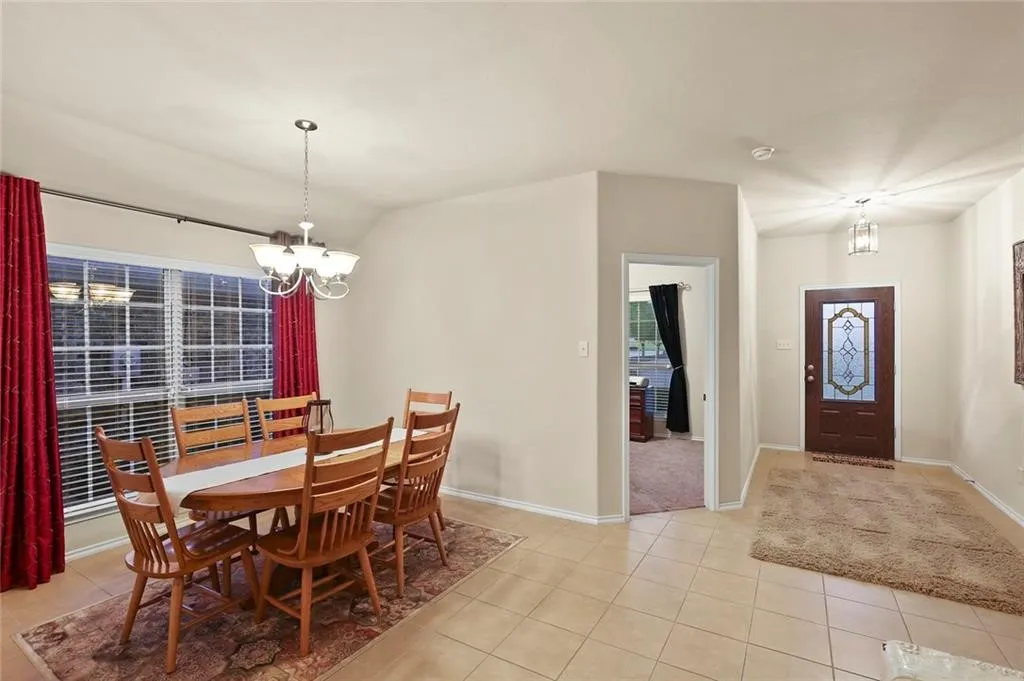 Entryway featuring a decorative glass front door and tile flooring, opening to a dining area with a multi-arm chandelier and a large window with blinds