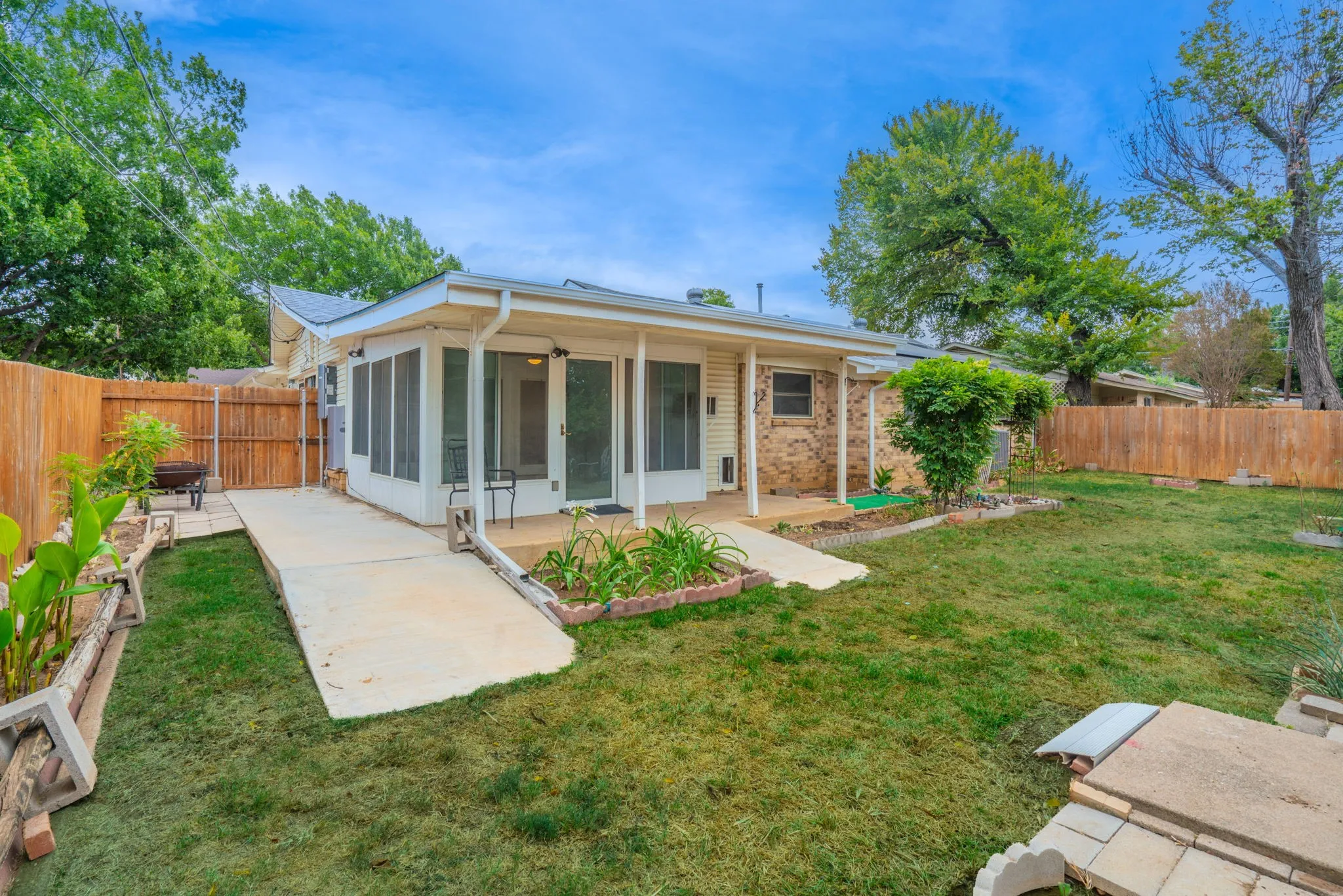 Expansive backyard with a covered patio, screen enclosure, concrete pathway, fenced perimeter, and mature landscaping