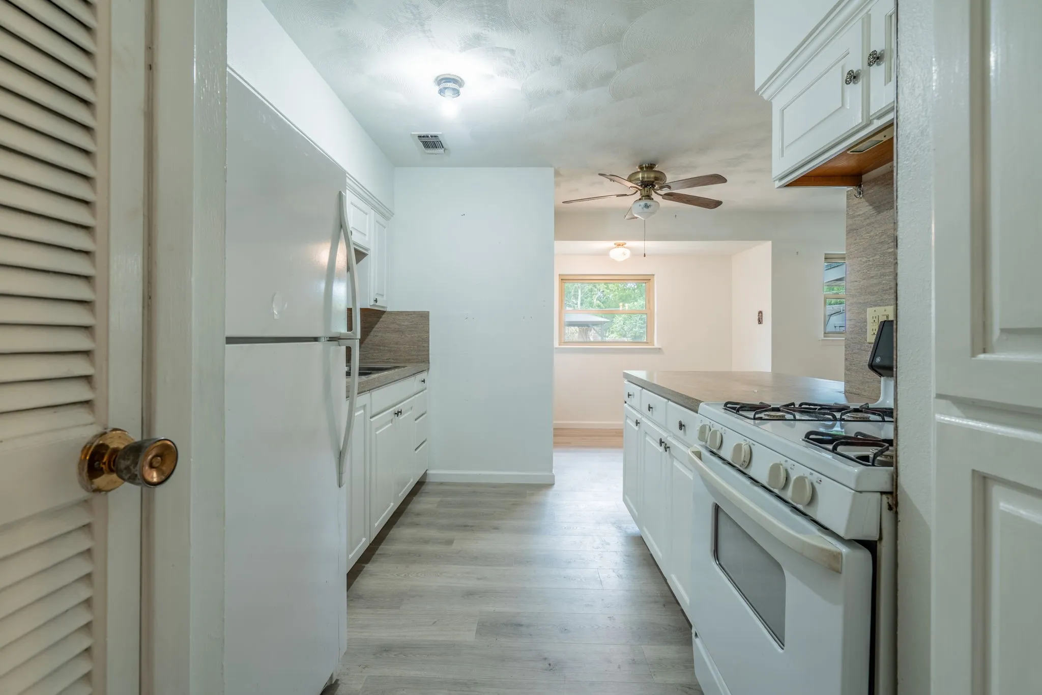 Kitchen featuring white cabinetry, light wood-finish flooring, a white refrigerator, a white range, and a ceiling fan in the adjacent space