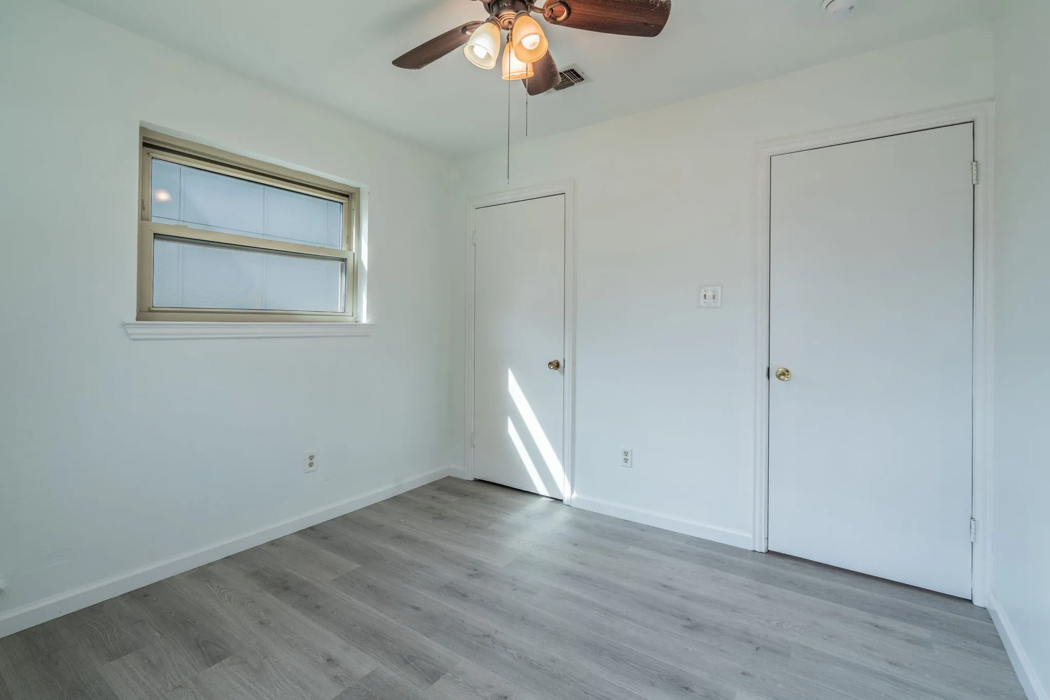 Light gray wood-finish flooring, crisp white walls, and a window with a white sill