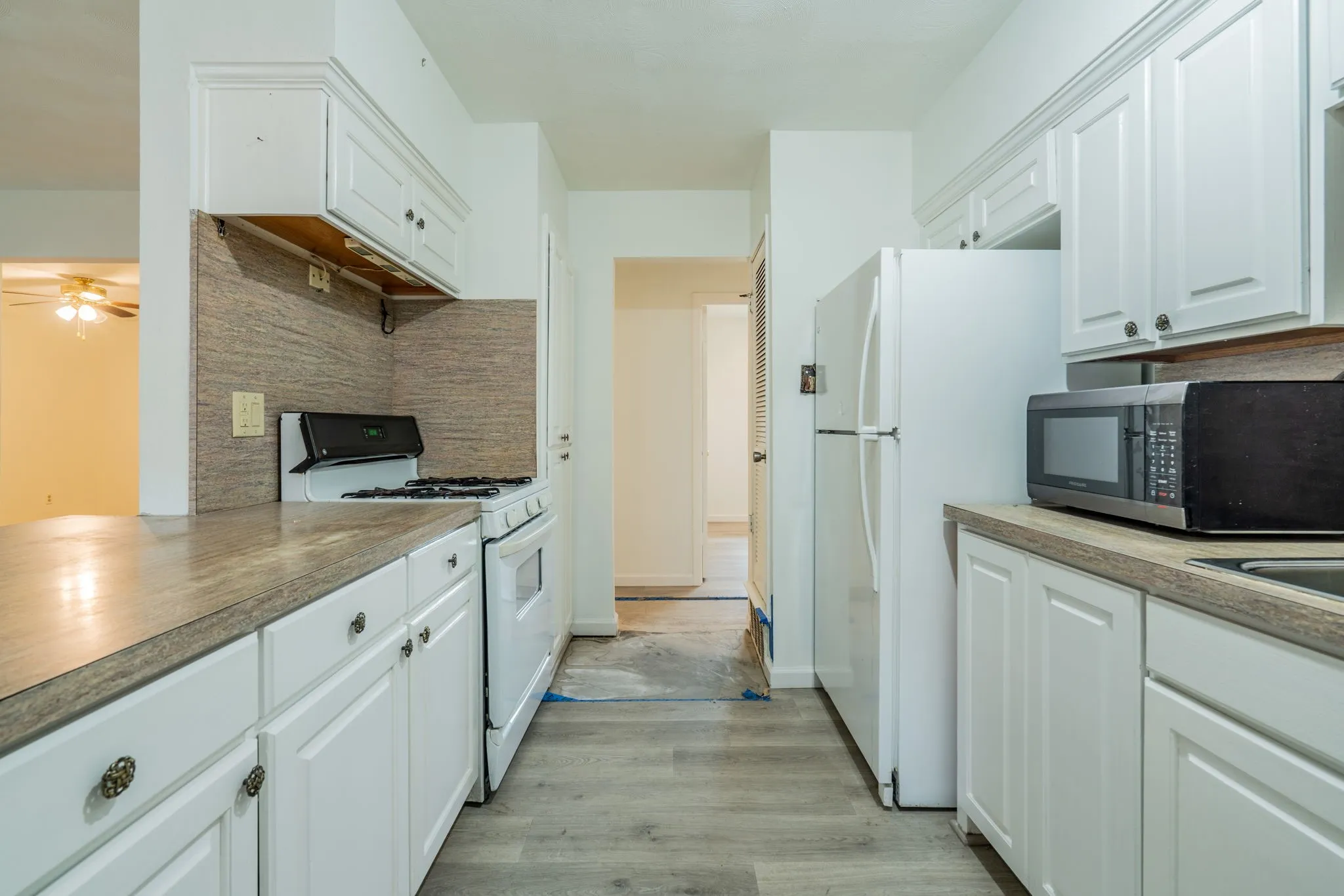 Galley kitchen featuring white cabinetry, light wood-finish flooring, and a stone-finish countertop