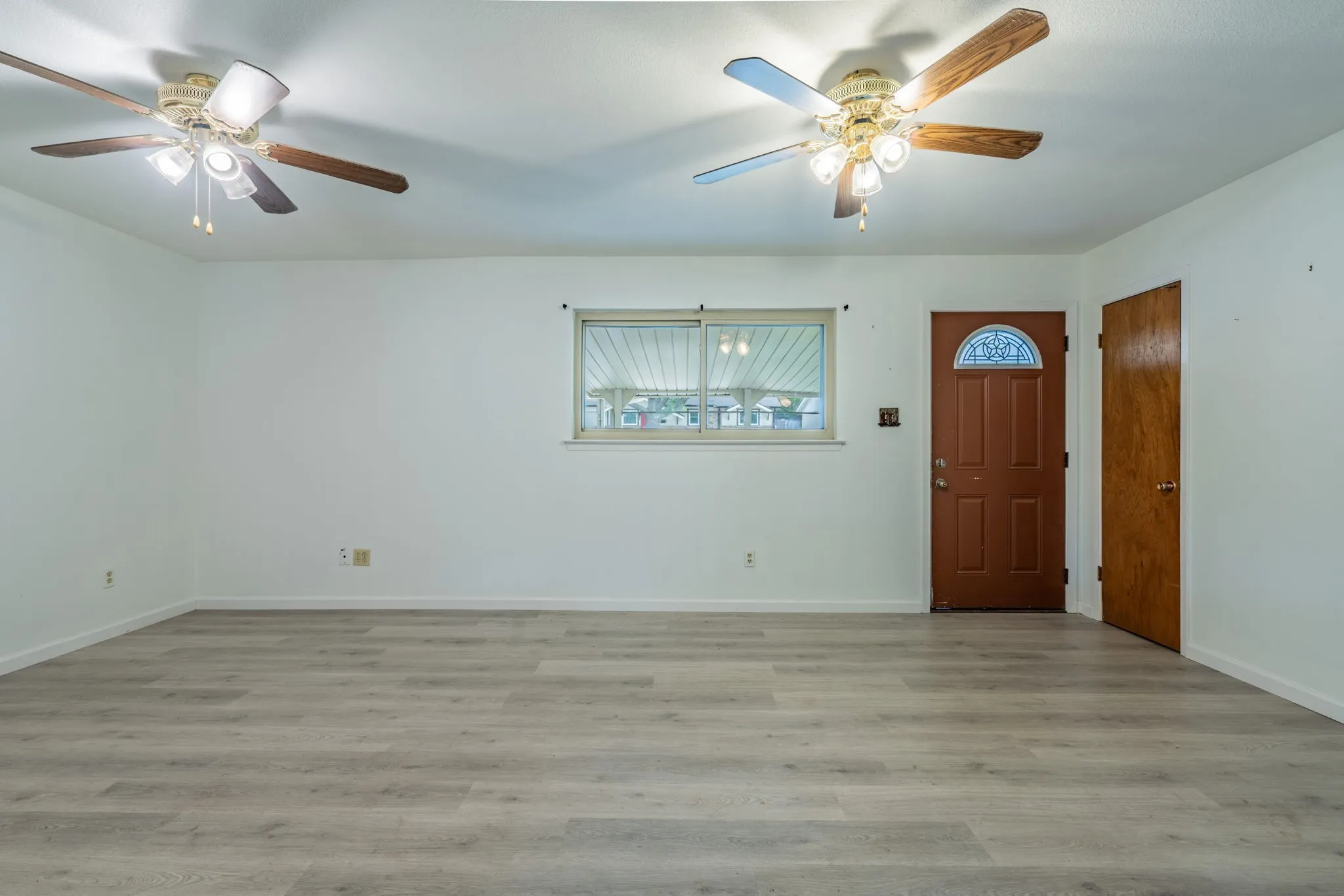 Spacious room featuring wood-finish flooring, two ceiling fans with lighting, and a window with white trim